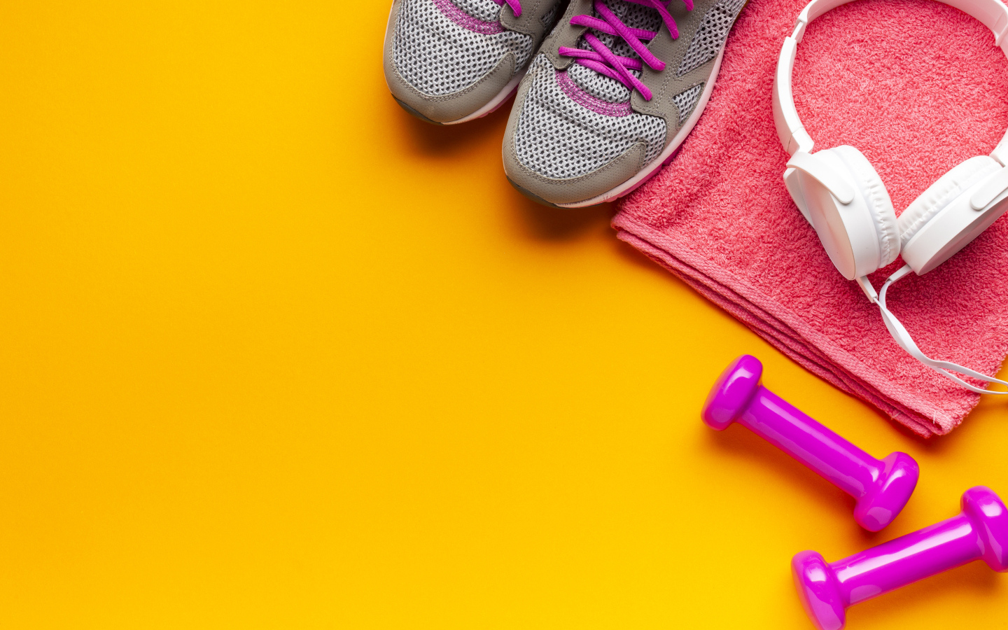 Розовые гантели, наушники, кроссовки и полотенце на желтом фоне