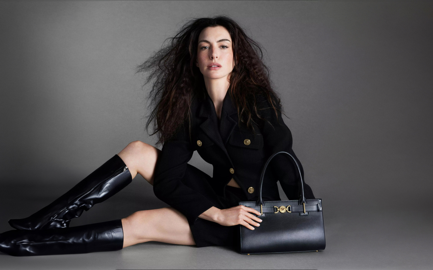 Актриса Энн Хэтэуэй в черных сапогах с сумочкой на сером фоне