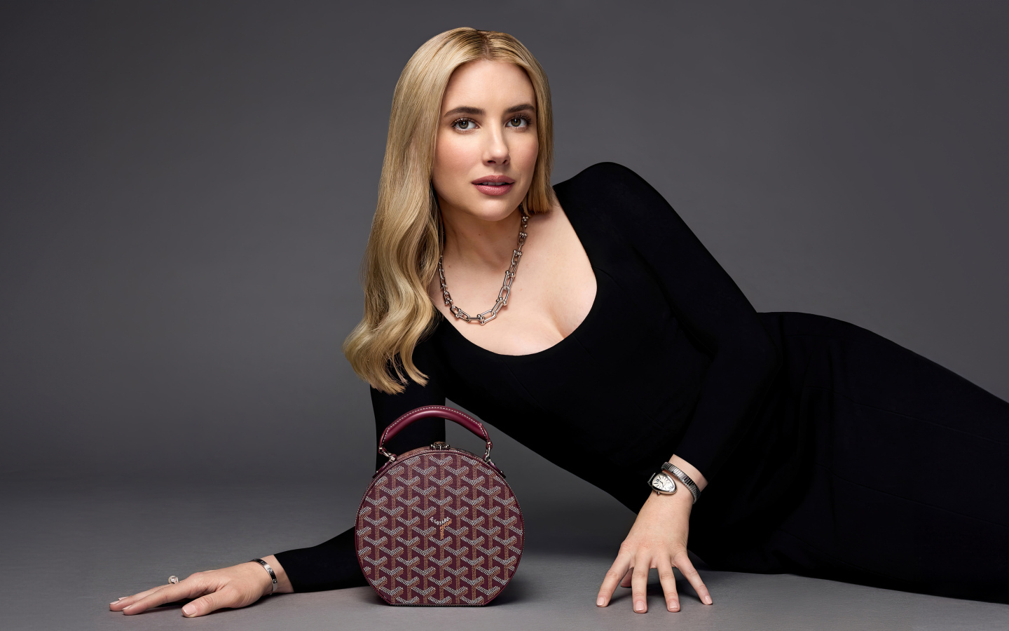 Актриса Эмма Робертс в черном платье с сумочкой лежит на сером фоне