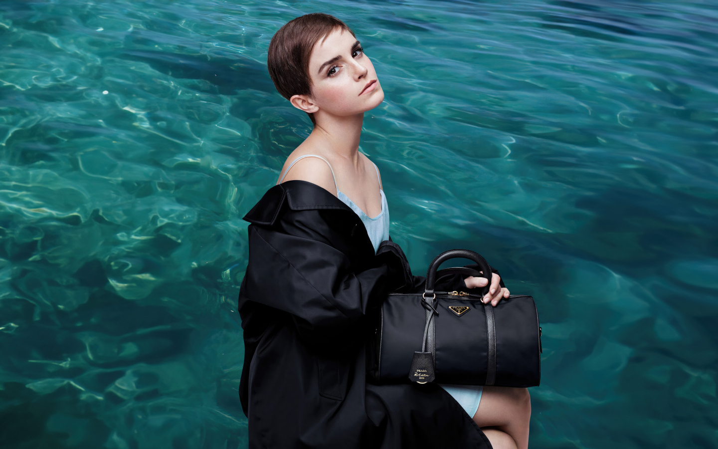 Актриса Эмма Уотсон с сумочкой сидит у воды