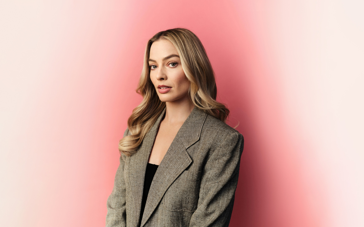 Актриса Марго Робби в сером пиджаке на розовом фоне