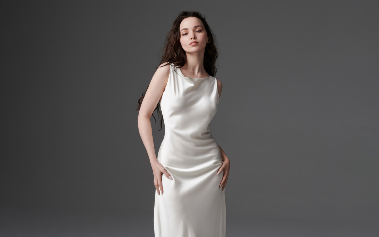 Стройная девушка актриса Дав Кэмерон в белом платье на сером фоне