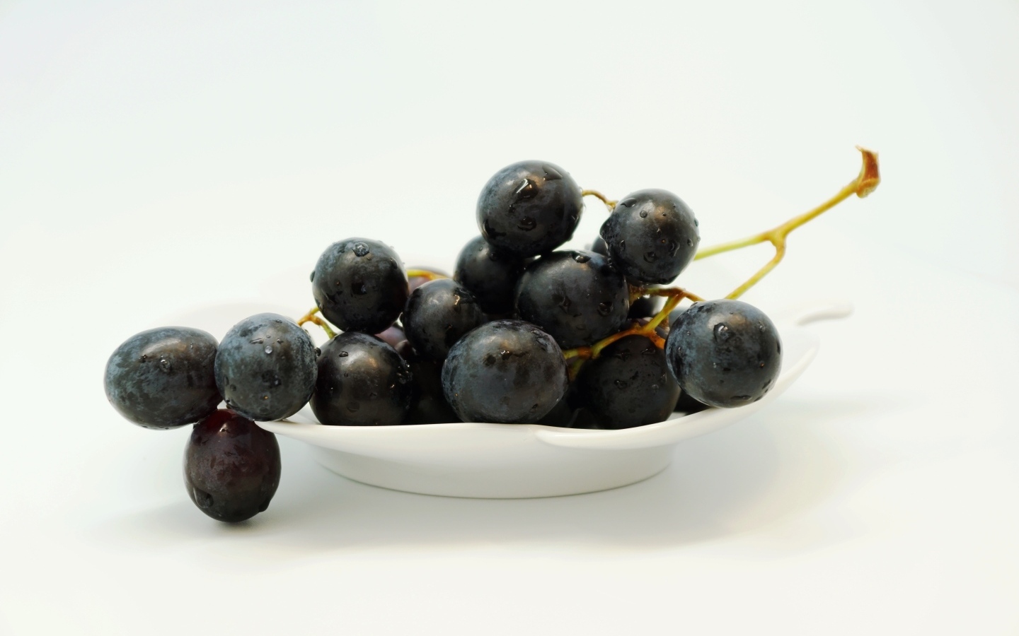 Гроздь синего винограда в тарелке на белом фоне