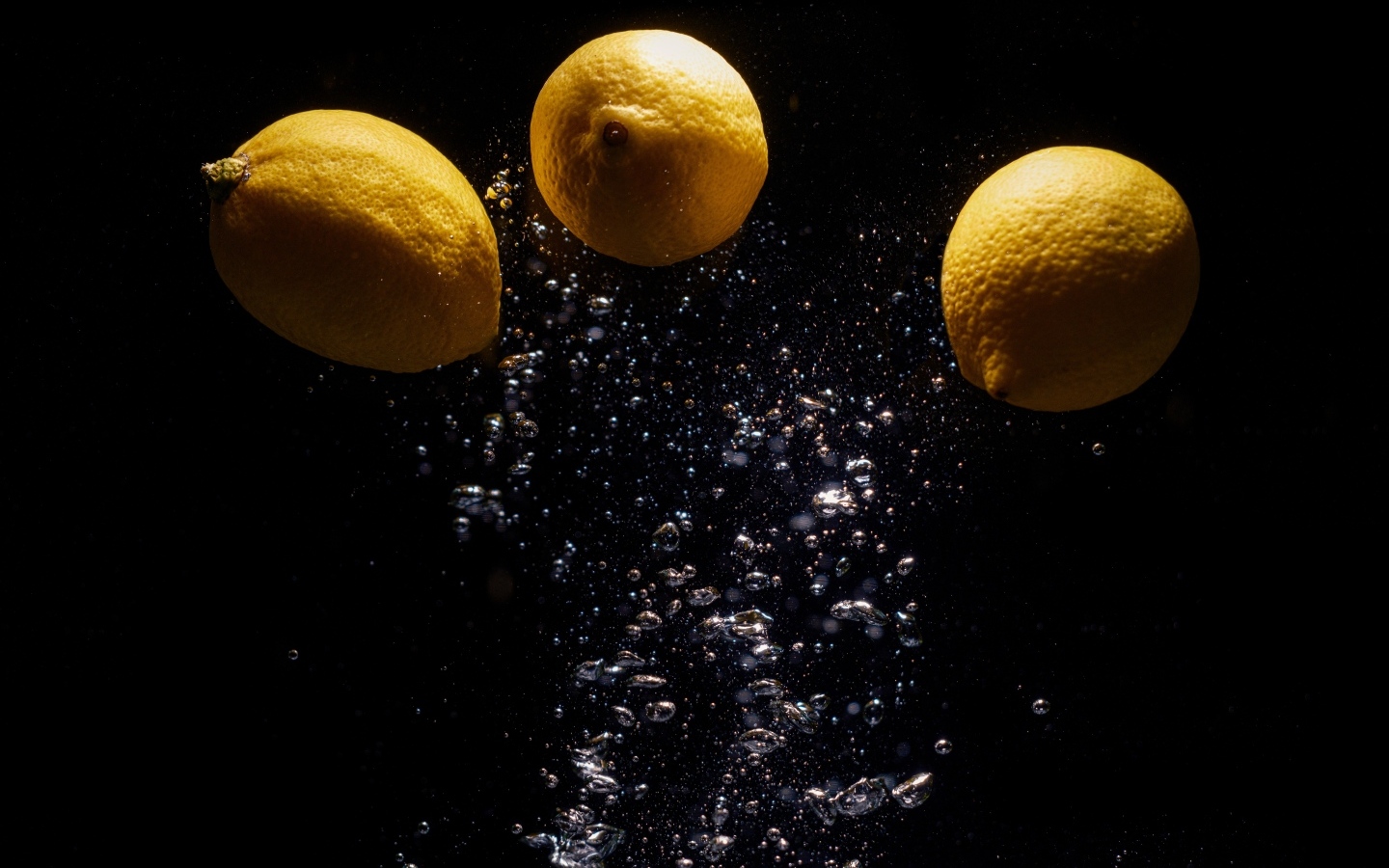 Три желтых лимона с пузырями в воде на черном фоне