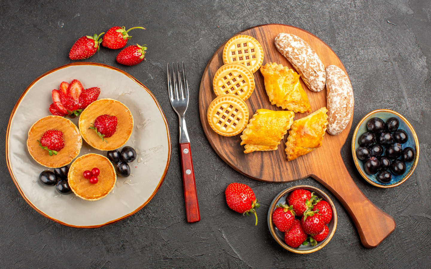 Печенье и оладьи на столе с ягодами клубники и виноградом