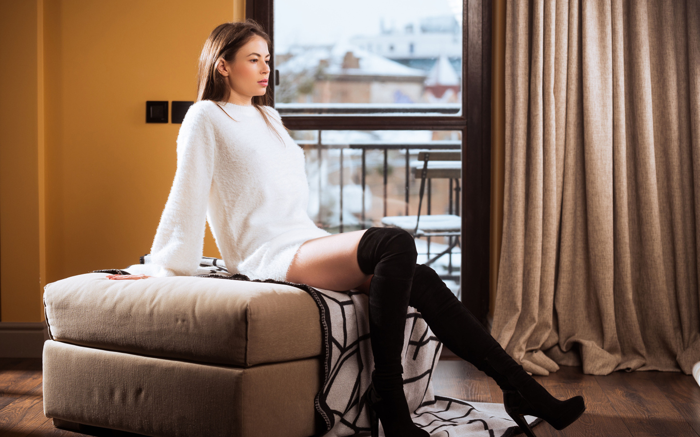 Девушка сидит на кресле в комнате у окна