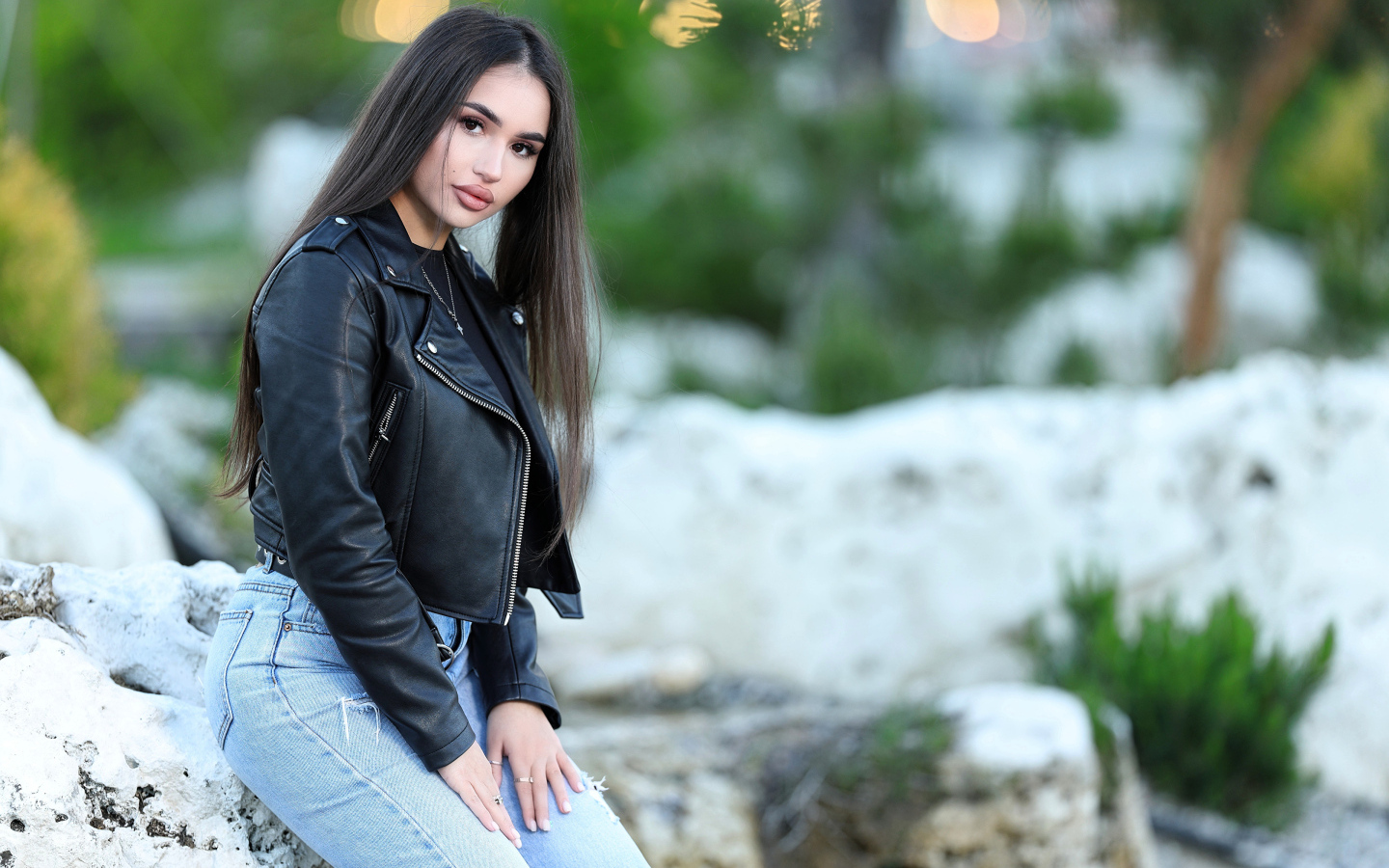 Брюнетка в черной кожаной куртке сидит на камне