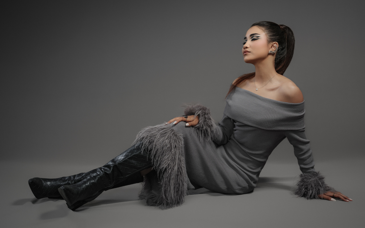 Девушка в платье и длинных черных сапогах на сером фоне