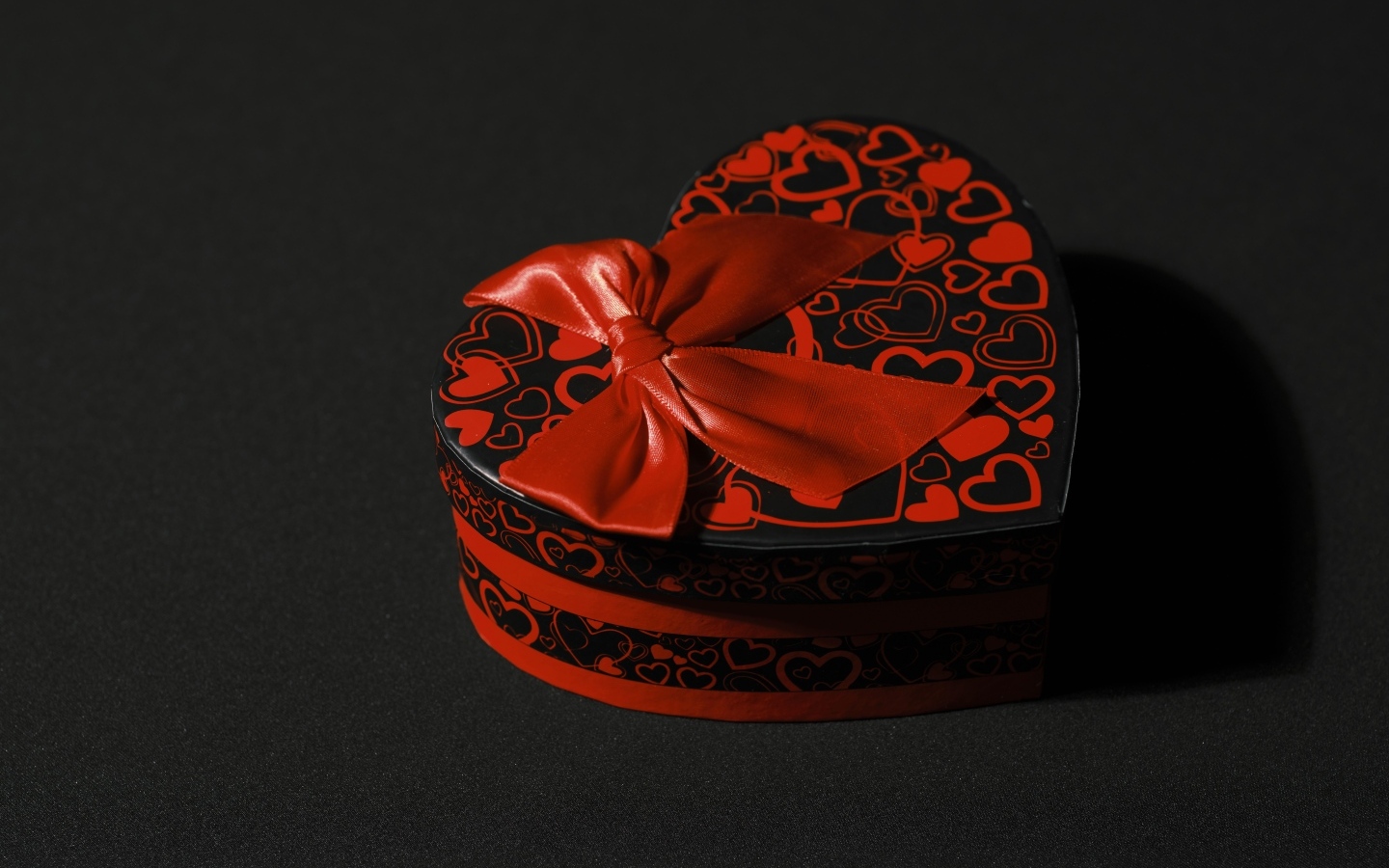 Heart shaped box with red bow on black background