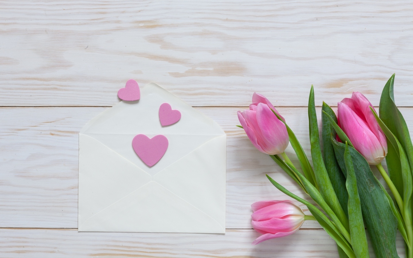 Розовые тюльпаны с конвертом с сердечками на деревянном фоне
