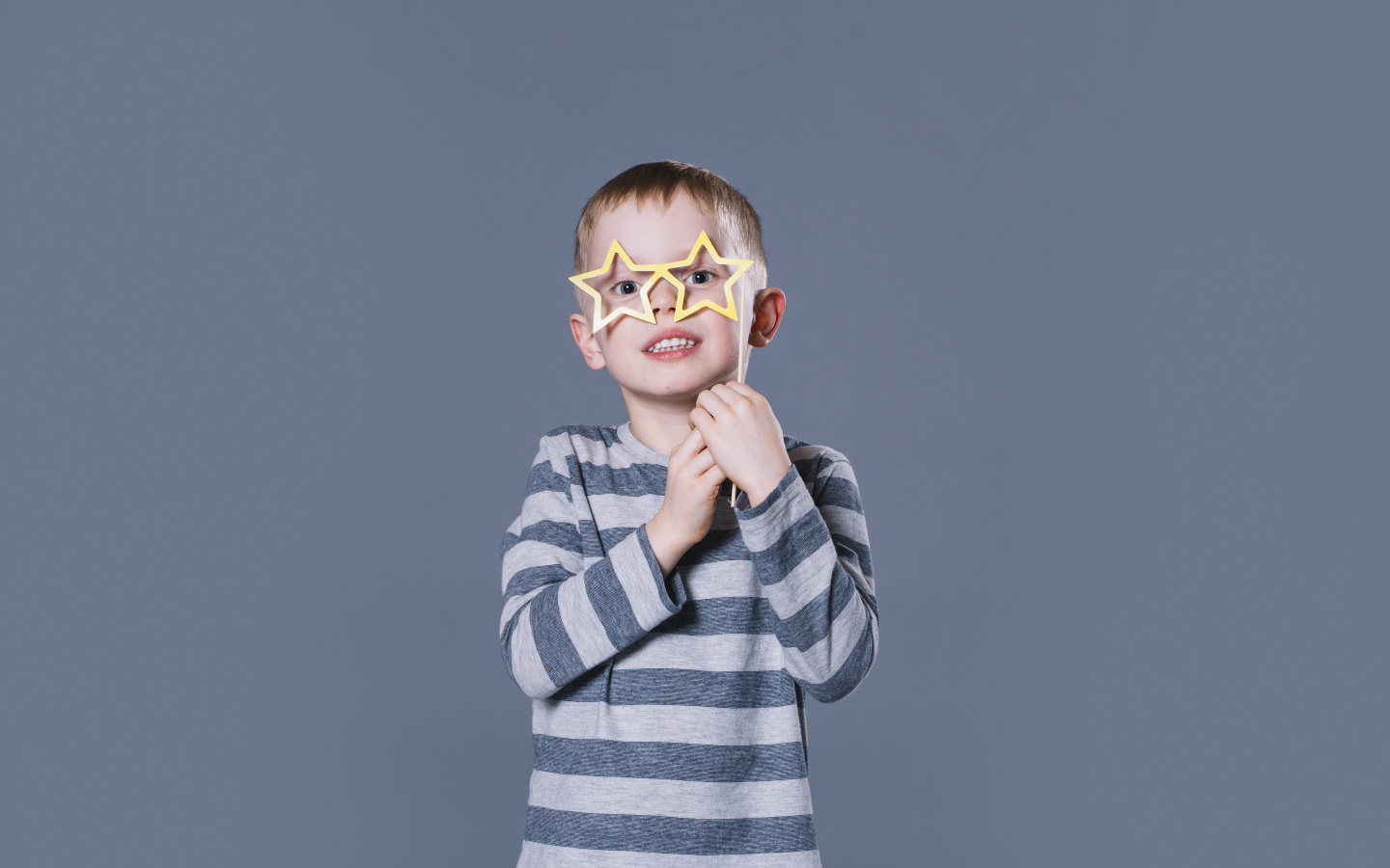Маленький мальчик с очками в форме звезд на сером фоне