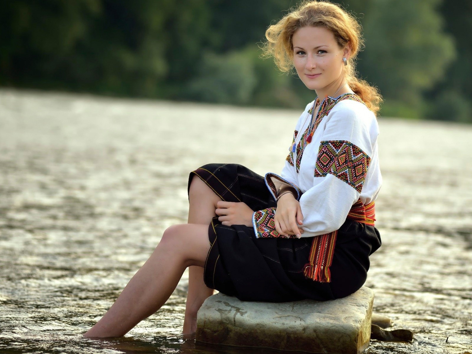 Девушка сидит на камне у воды в традиционном наряде
