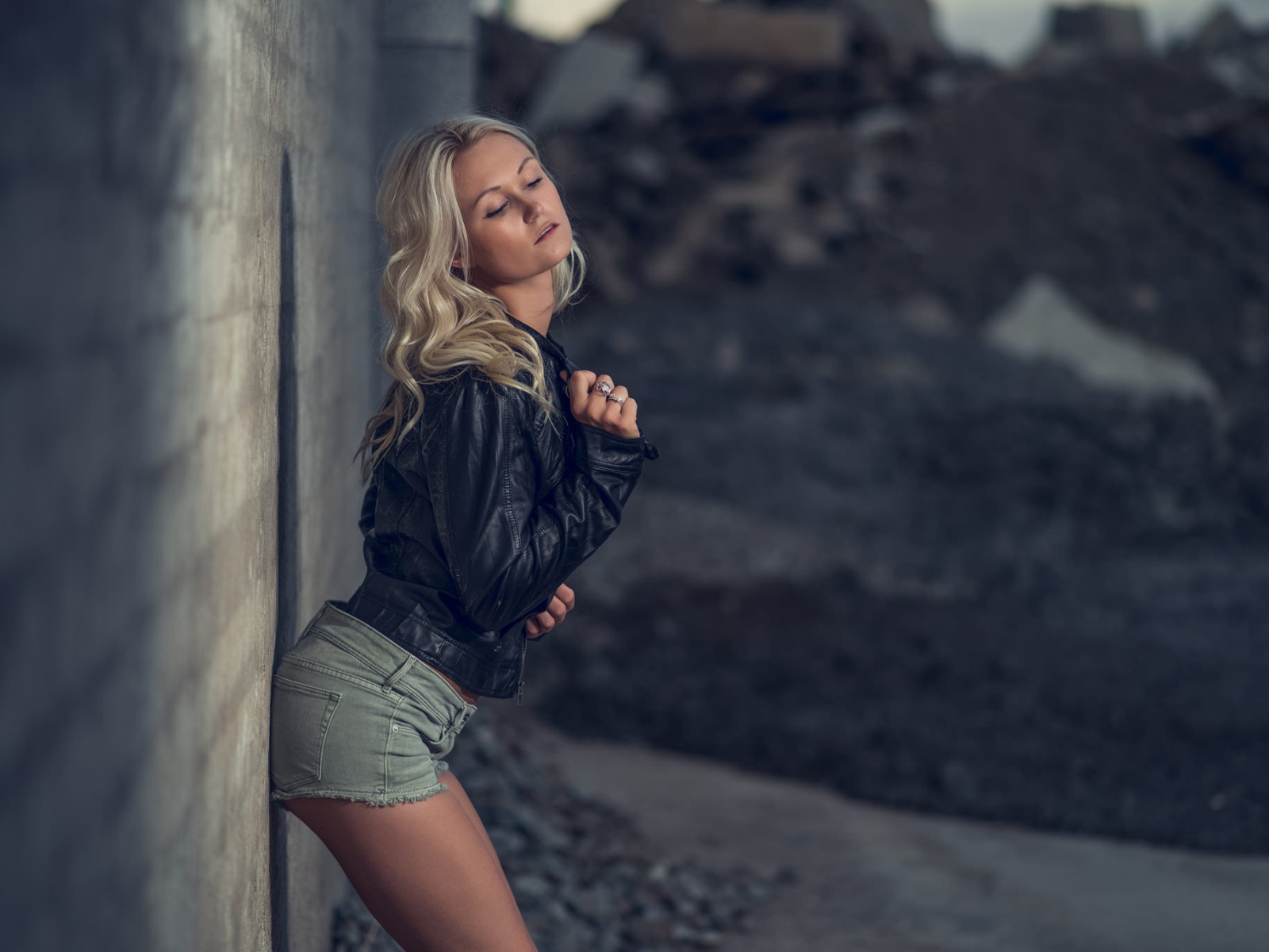 Блондинка в джинсовых шортах стоит у стены
