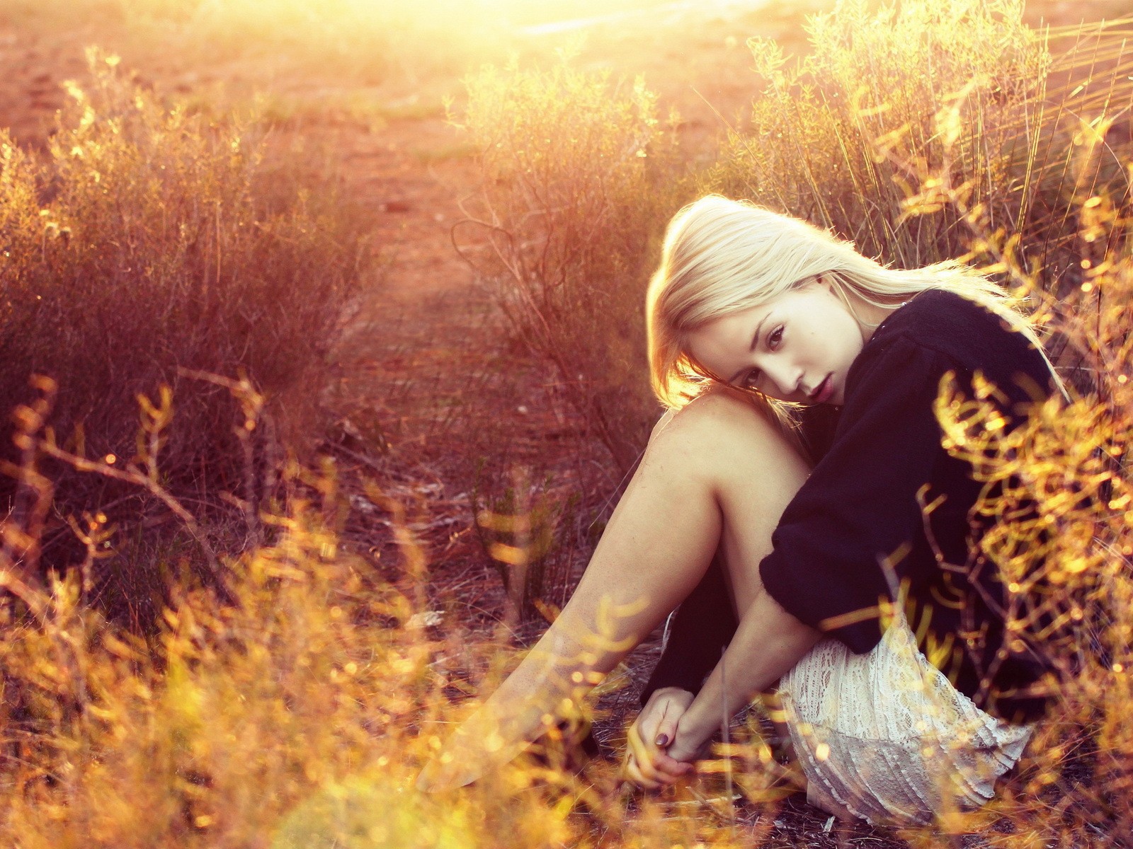 Блондинка сидит среди кустарников