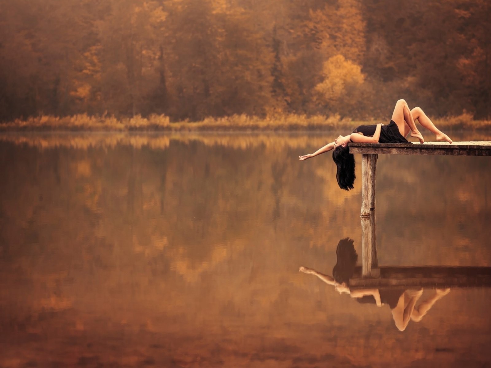 Брюнетка лежит на пирсе на озере