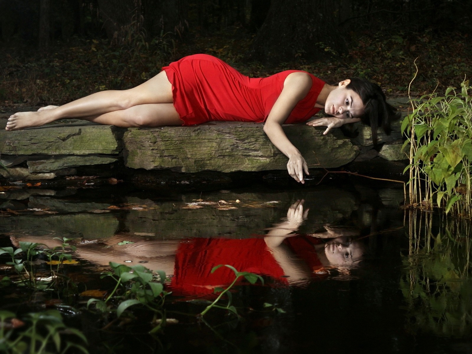 Девушка в красном платье лежит на камне у водоема