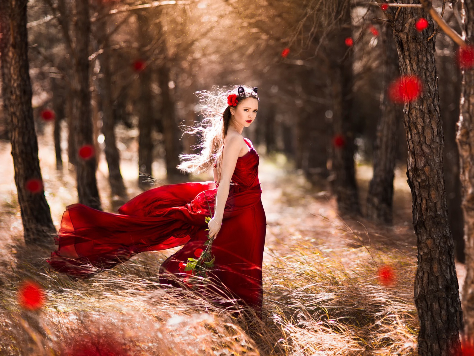 Девушка в красном платье стоит в ветренном лесу