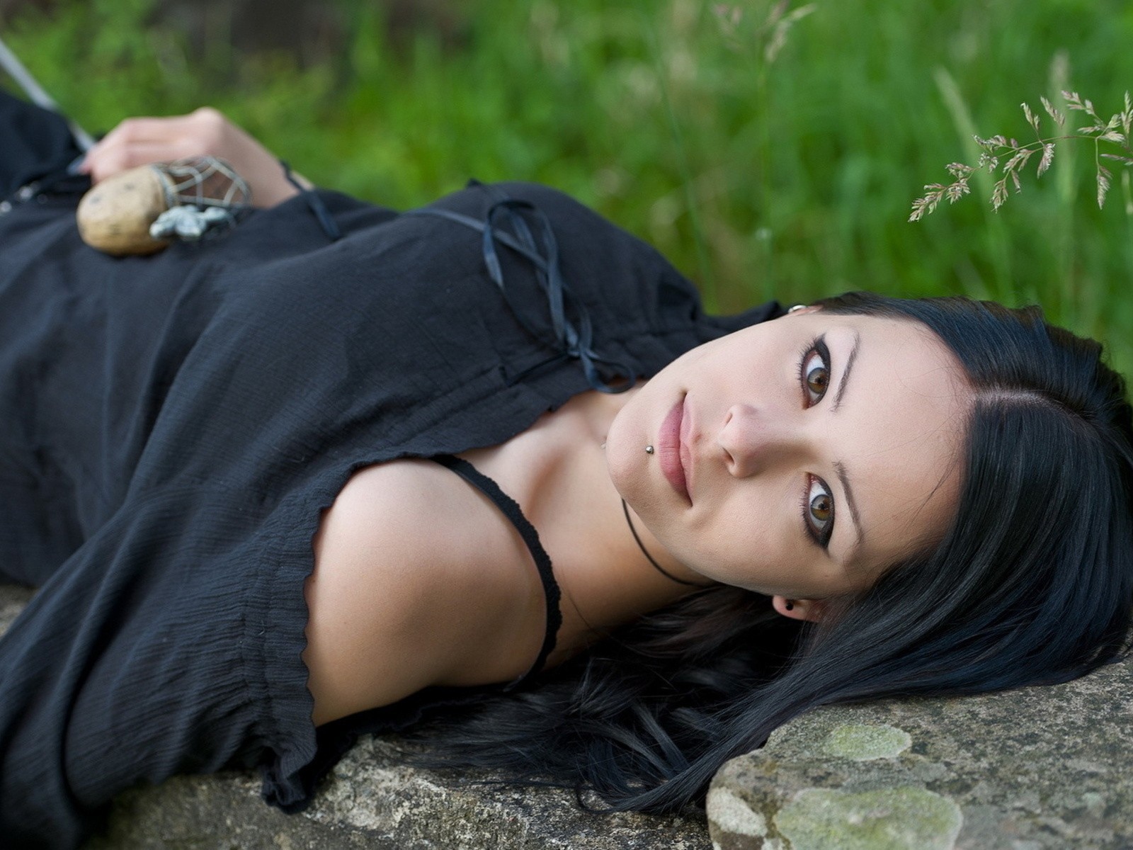 Модель в черном платье лежит на камне в траве