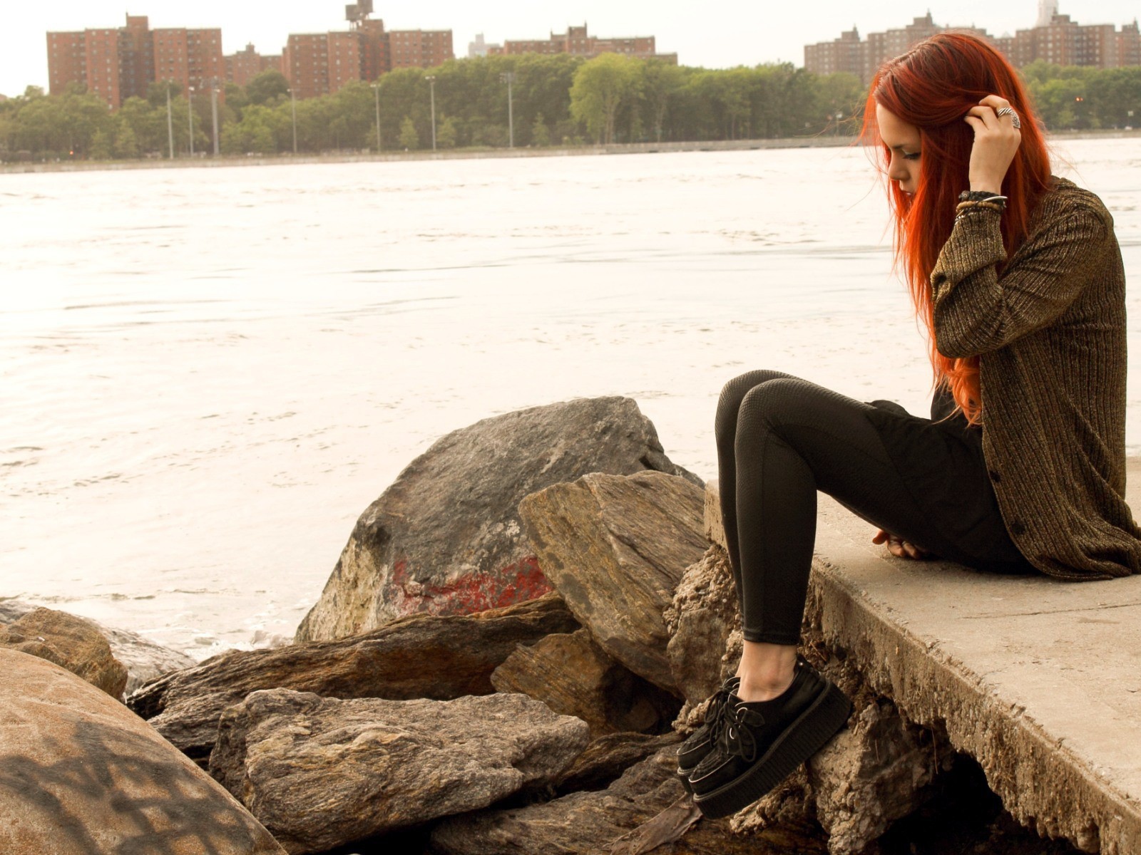 Рыжая девушка сидит на плитах набережной