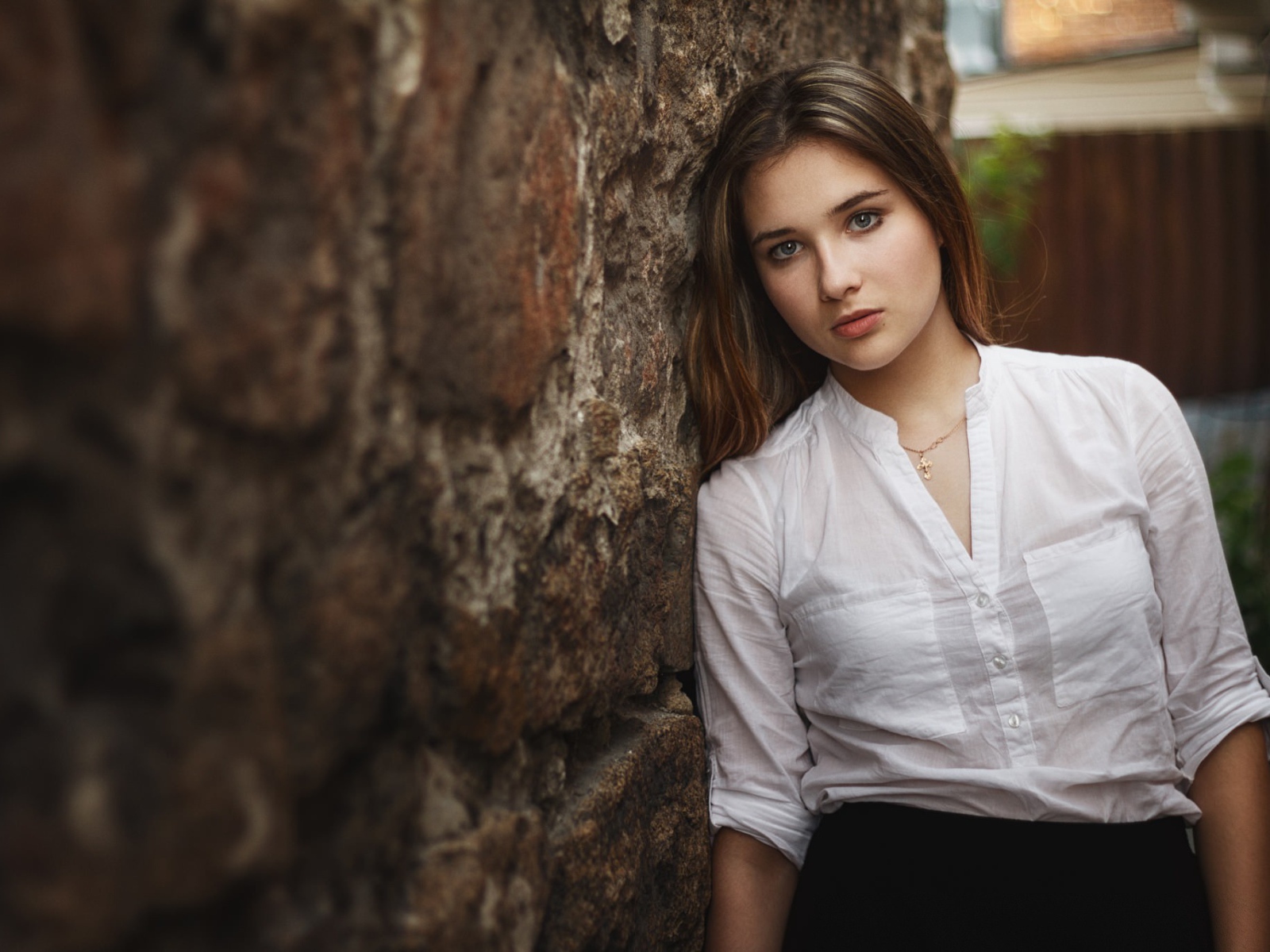 Девушка в белой рубашке стоит у стены