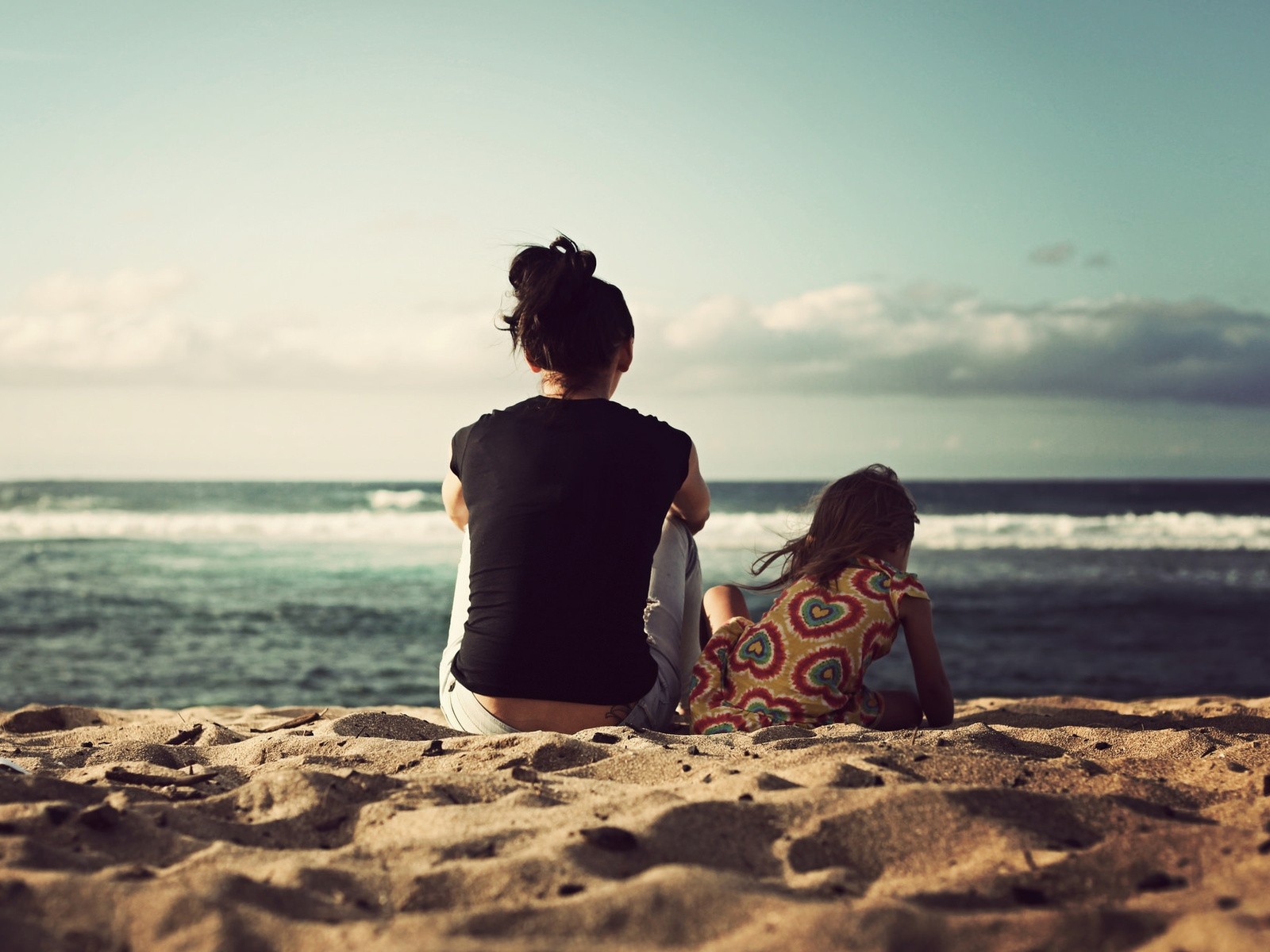 A woman and her daughter sitting in the sand on the beach