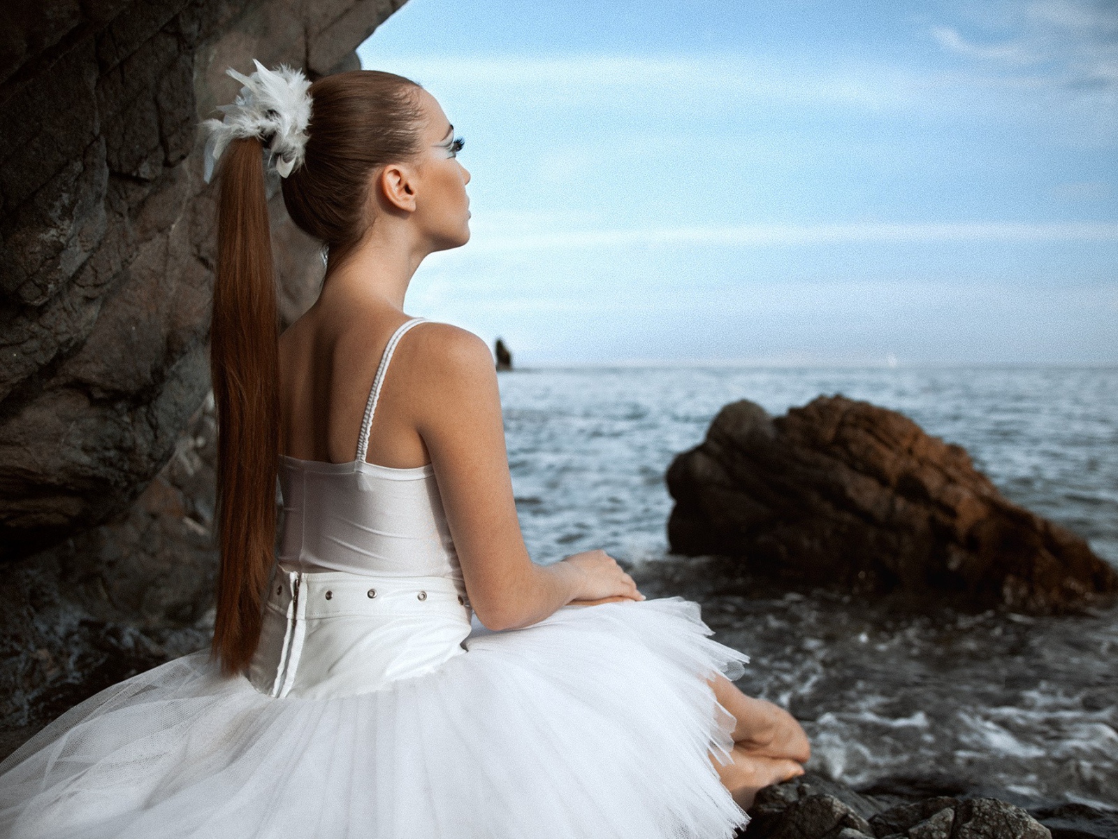 Балерина в белом платье сидит на берегу моря