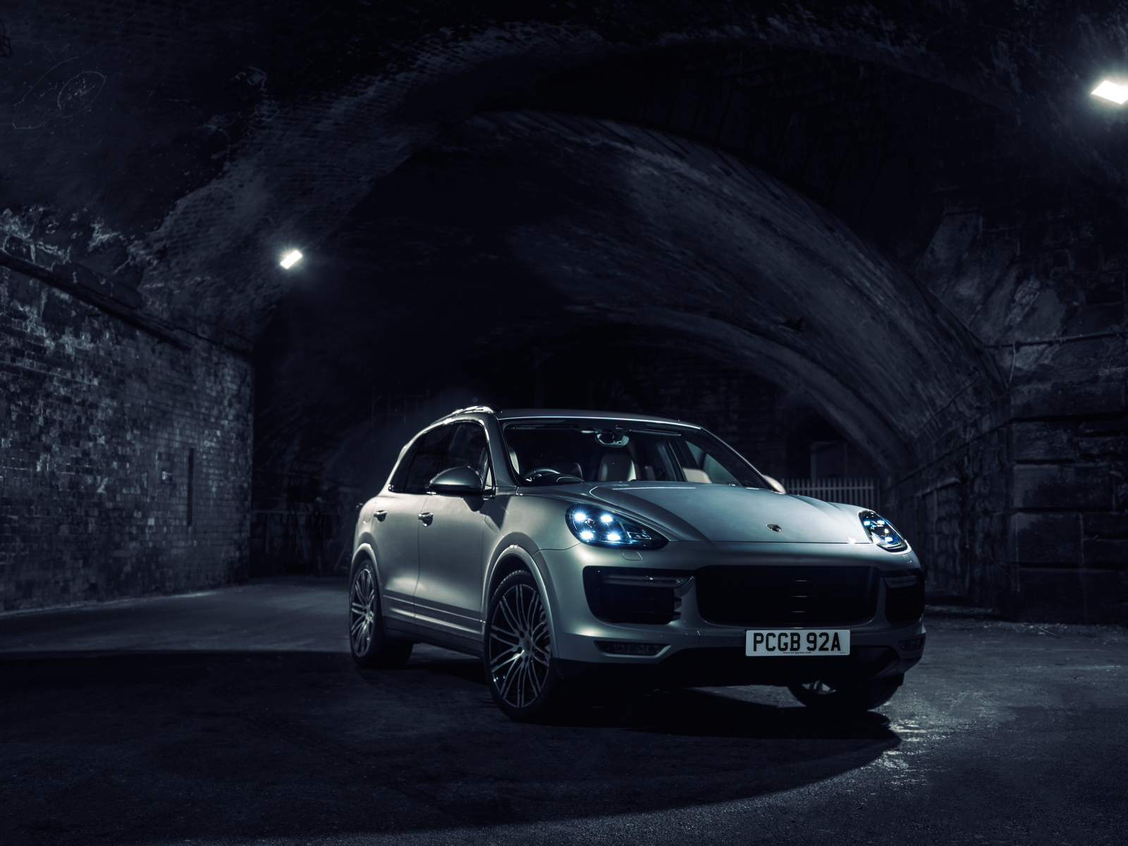 Серебристый автомобиль Porsche Cayenne в тоннеле с включенными фарами