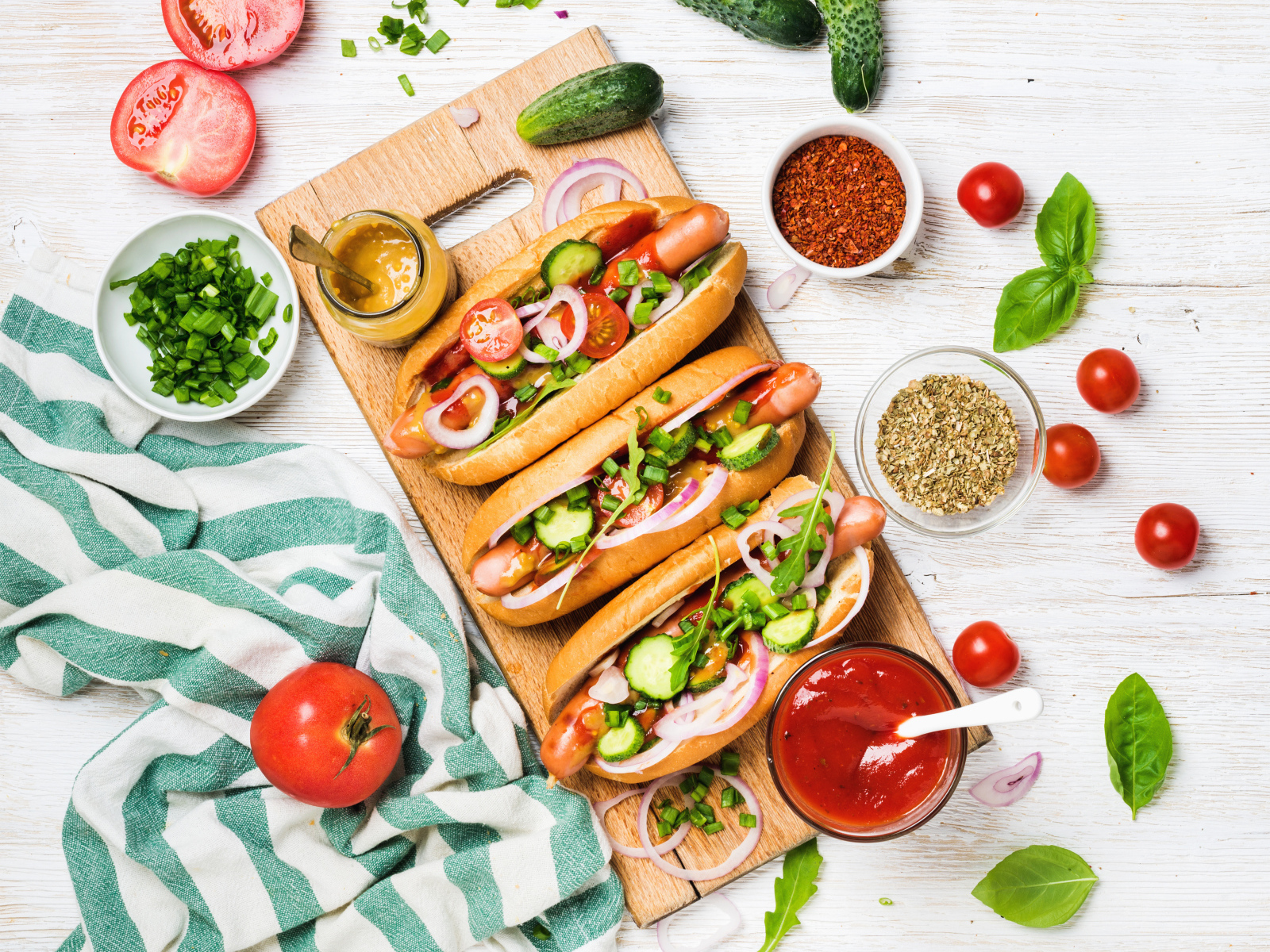 Аппетитные хотдоги на разделочной доске с овощами