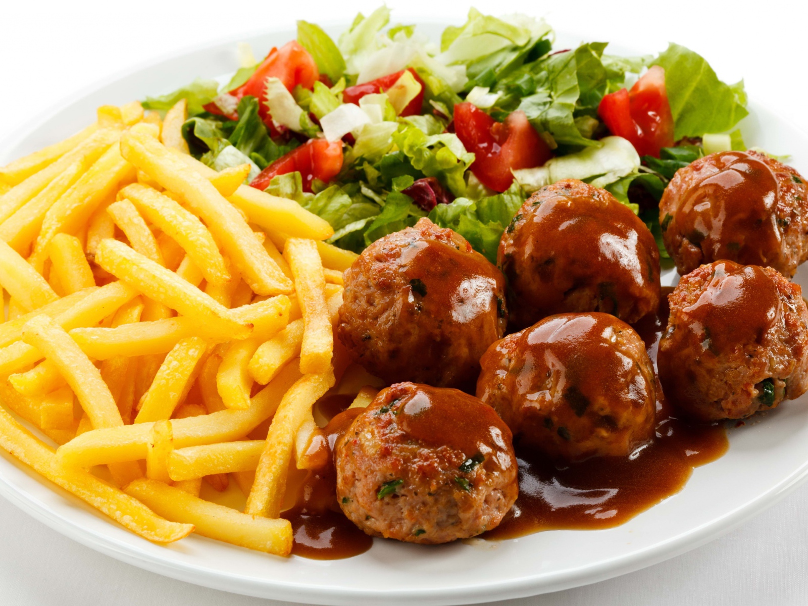 Картофель фри на белой тарелке с салатом и фрикадельками