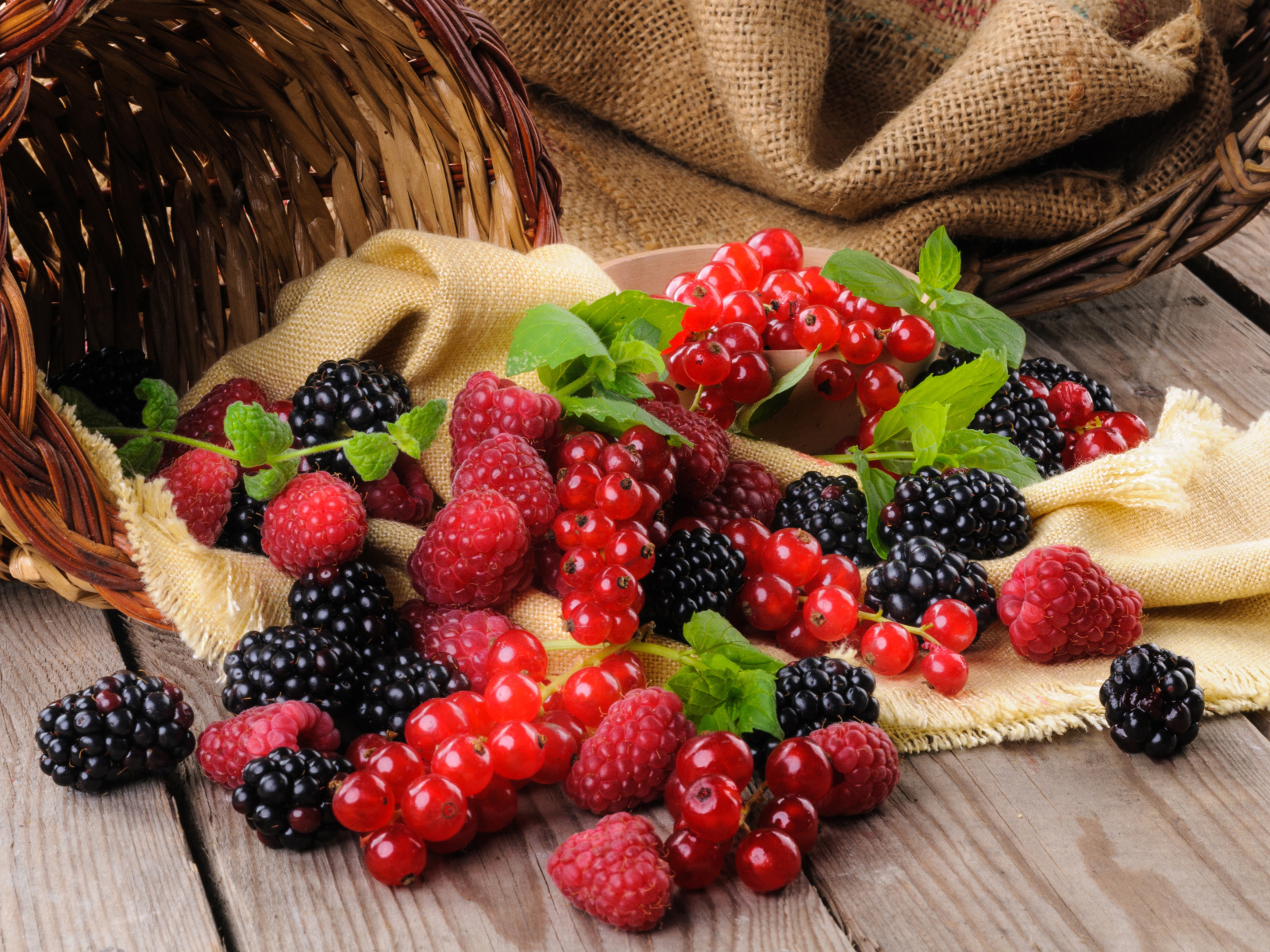 Свежие ягоды ежевики, малины и красной смородины с корзиной на столе
