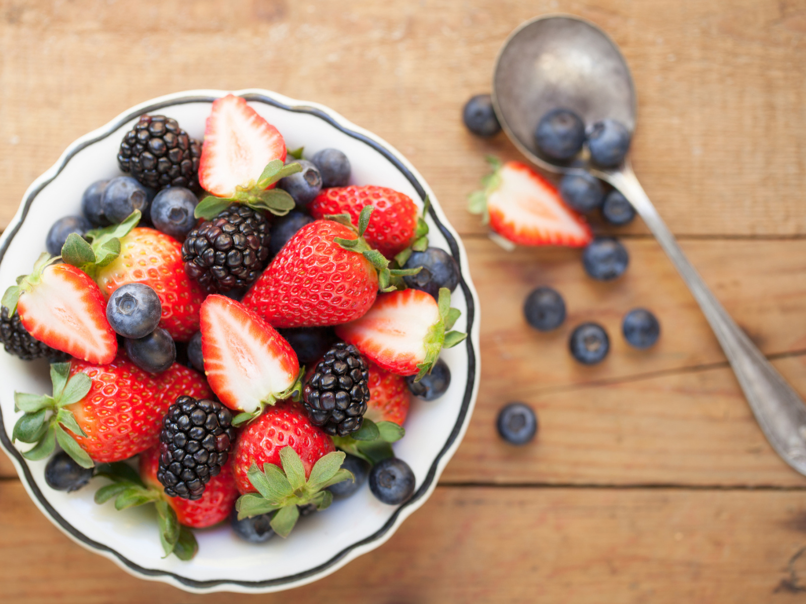 Свежие ягоды клубники, черники и ежевики в тарелке на деревянном столе