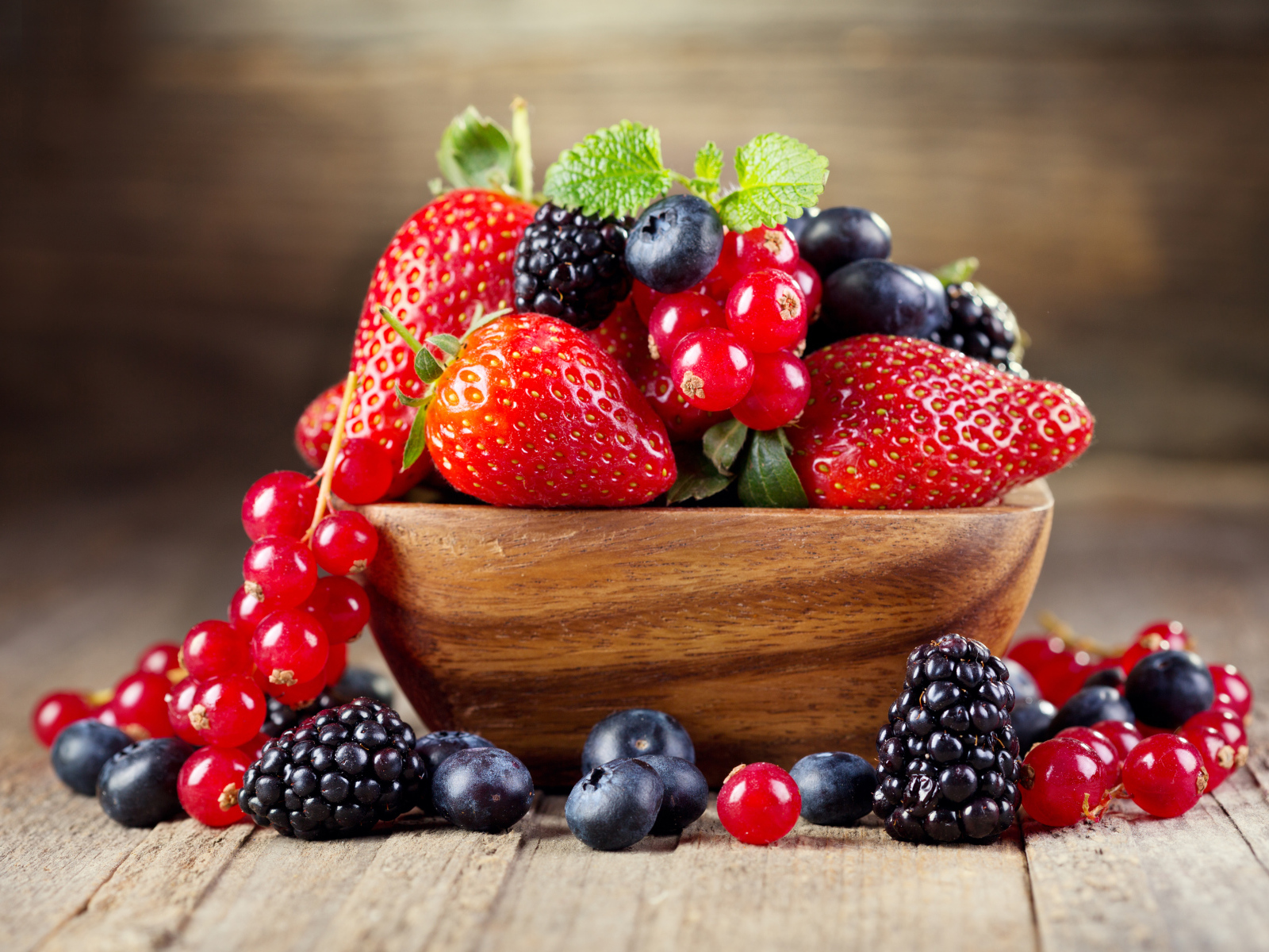 Свежие ягоды смородины, черники и клубники в деревянной тарелке на столе