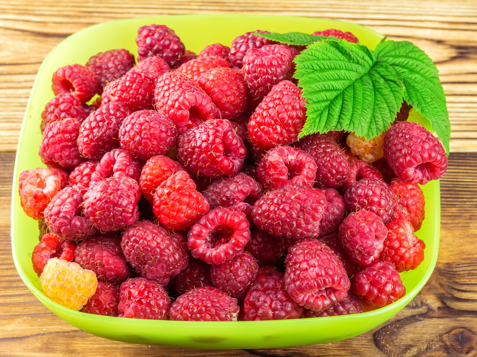 Свежая малина в зеленой миске на столе
