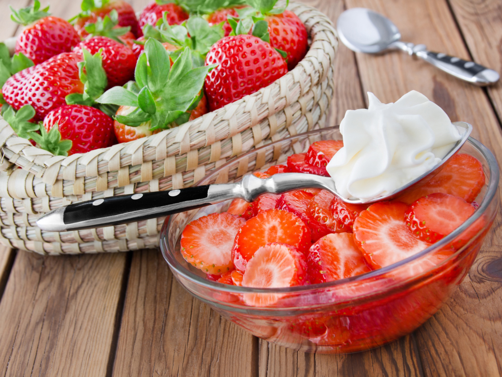 Нарезанная клубника в стеклянной посуде с ложкой сливок