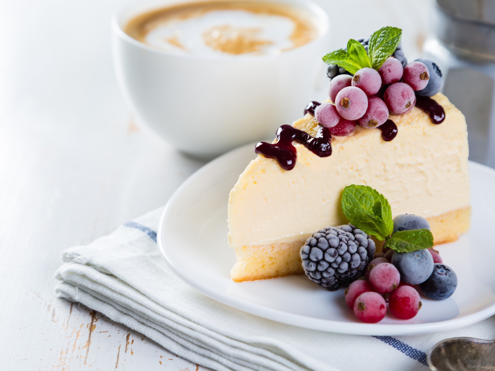 Кусок чизкейка с замороженными ягодами и чашкой кофе на столе