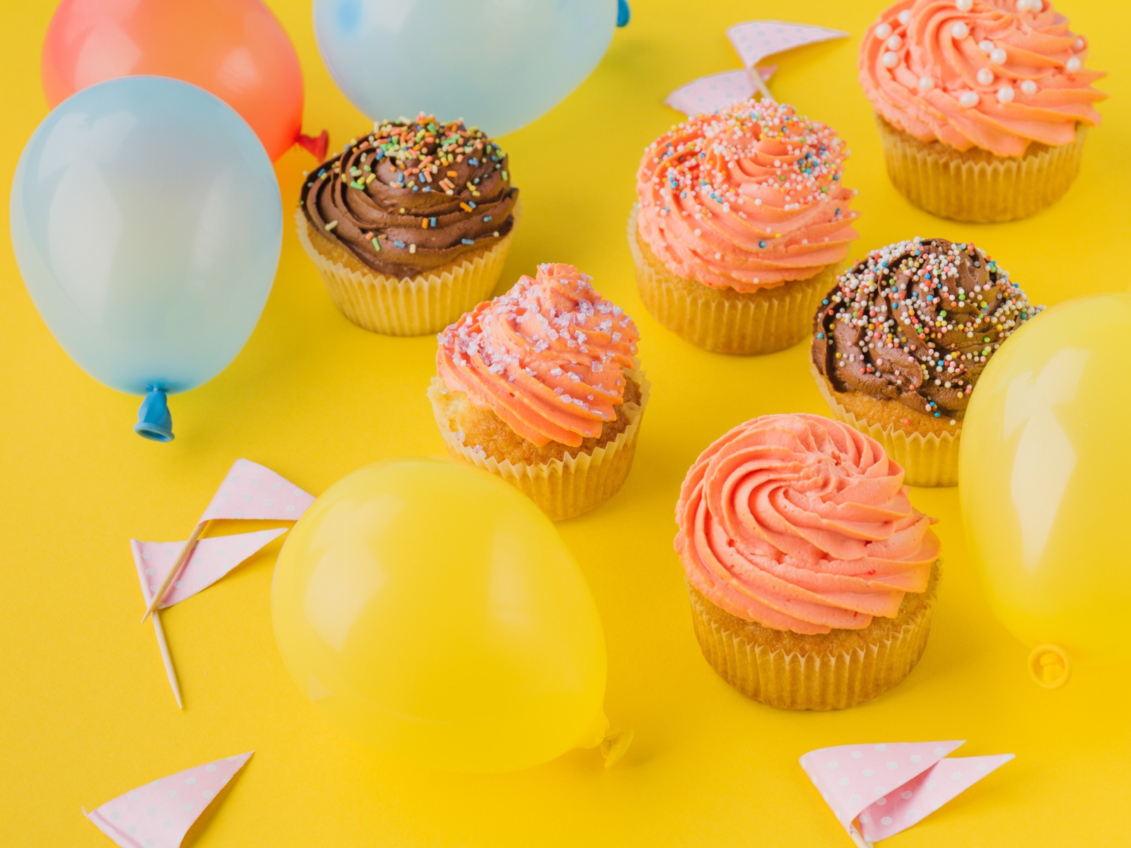 Аппетитные капкейки с кремом и воздушными шариками на желтой поверхности