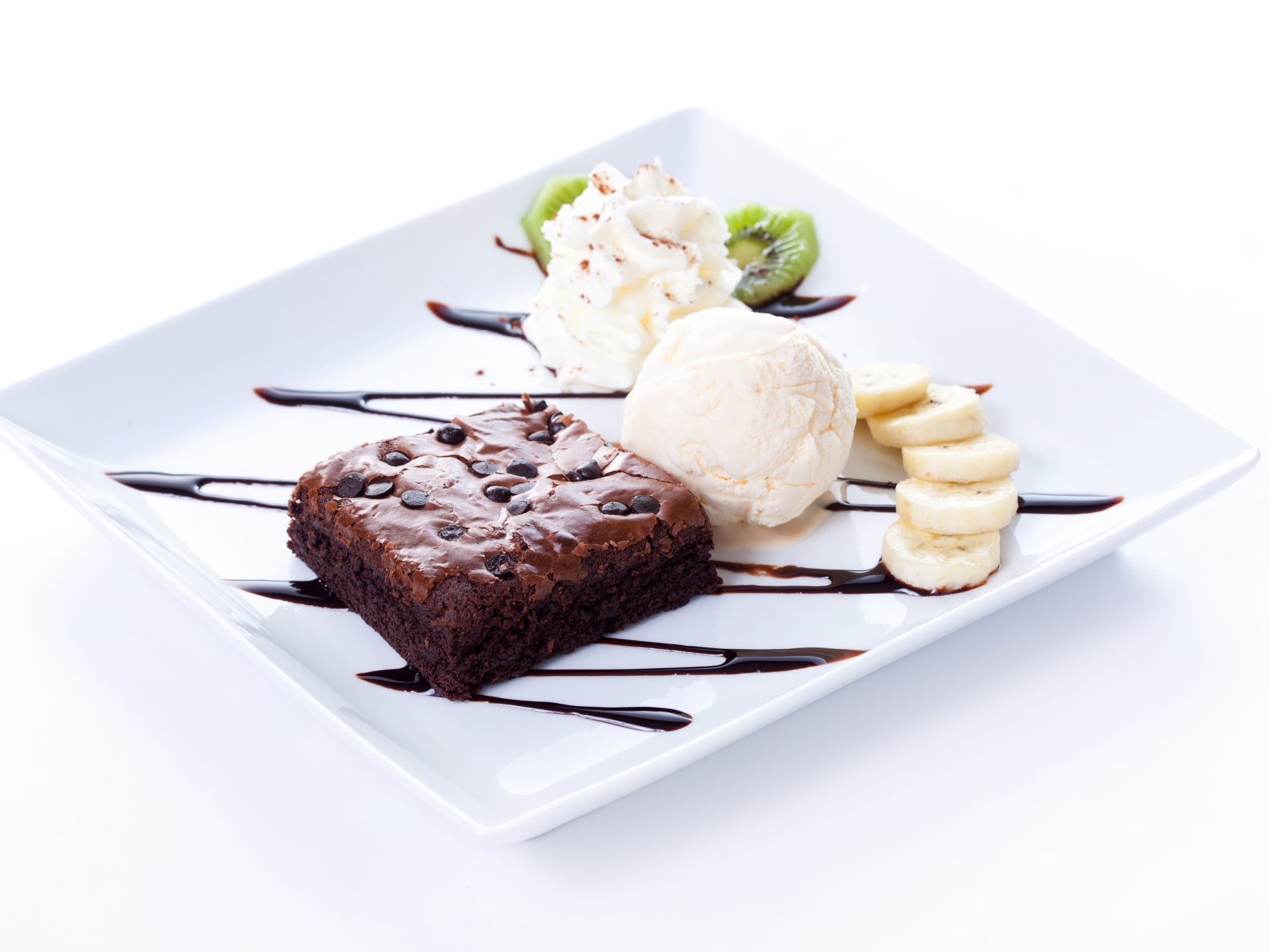 Шоколадное пирожное с мороженым, сливками и кусочками банана на белой тарелке