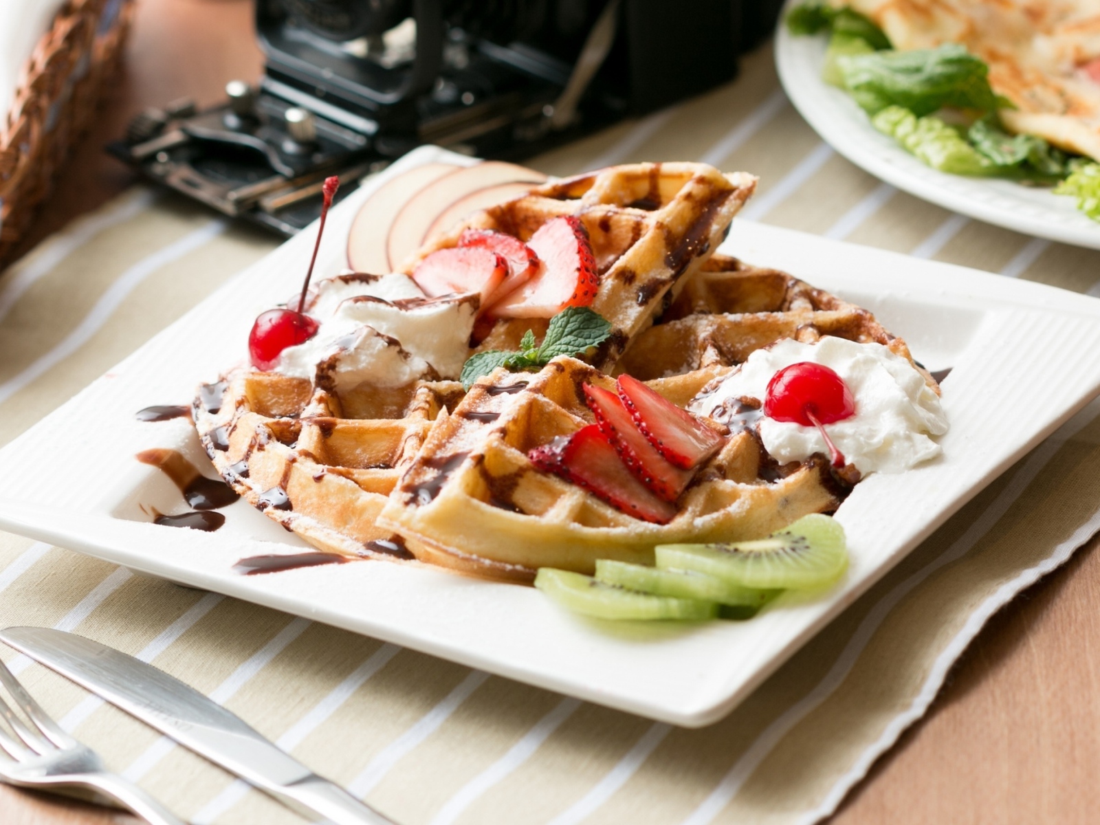 Сладкие вафли с ягодами клубники, вишни и кусочками киви на тарелке