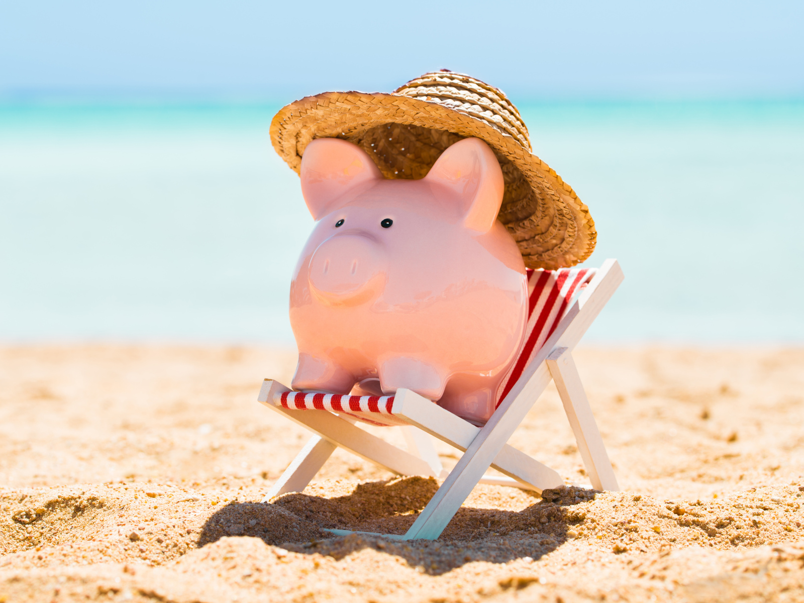 Сувенир свинка в шляпе лежит в игрушечном кресле на пляже