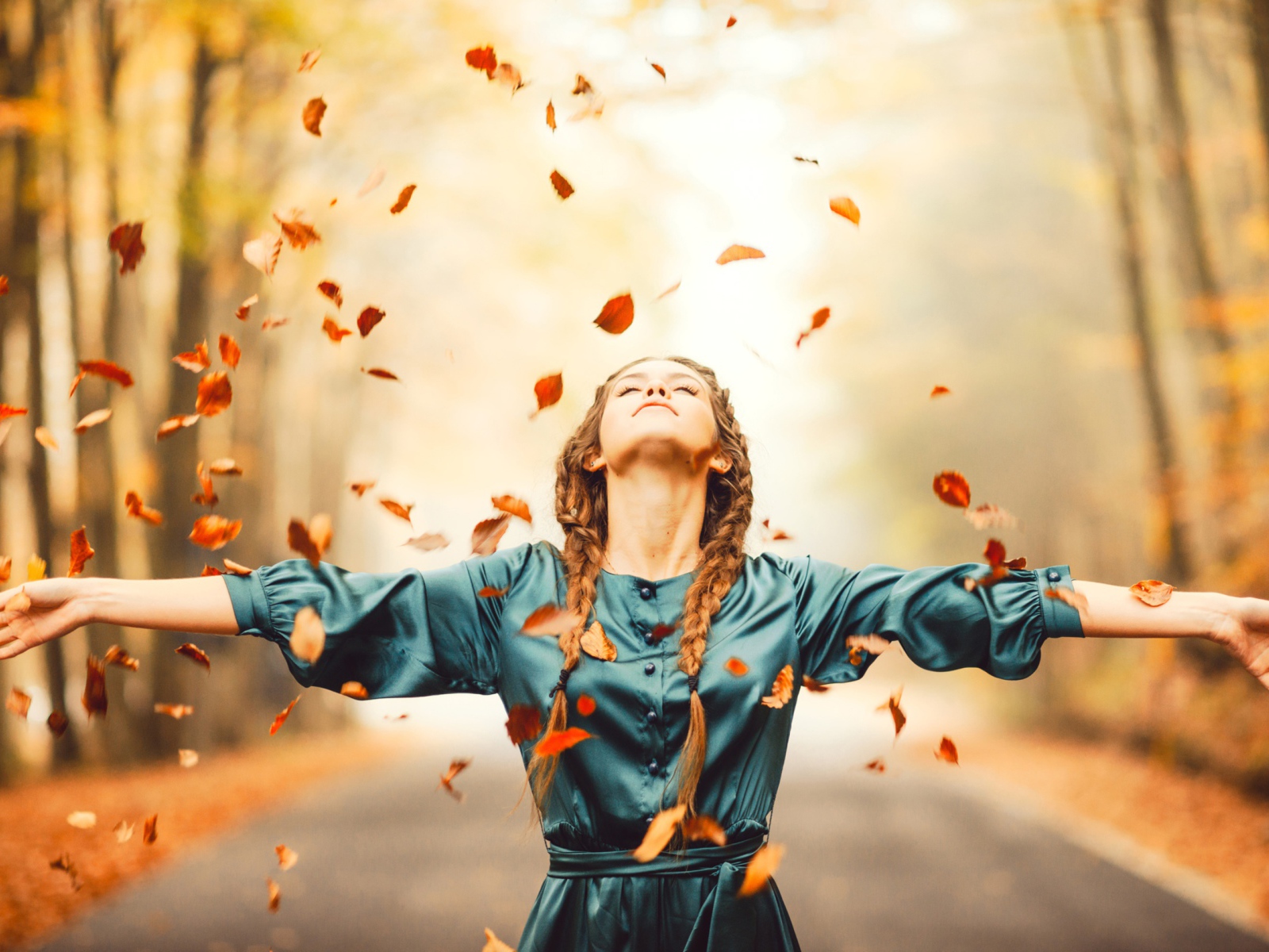 Красивая девушка с косичками подбрасывает желтые листья осенью