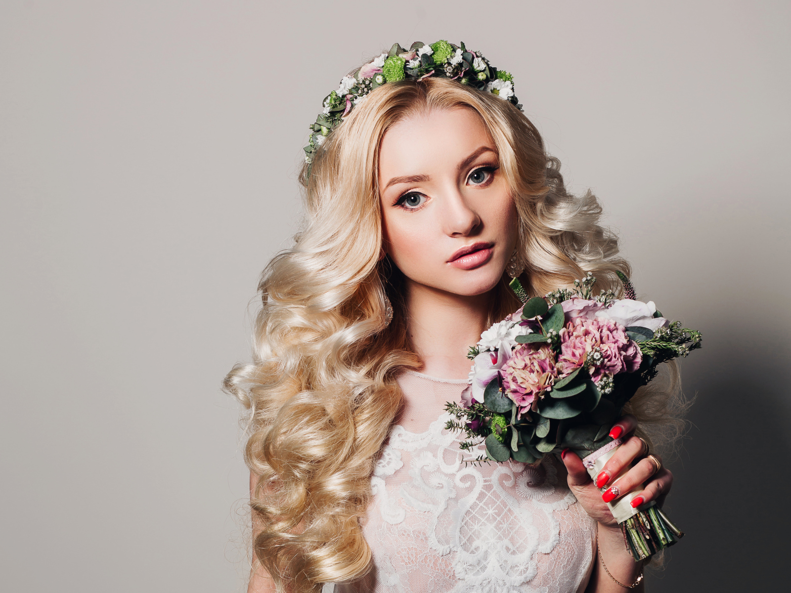 Красивая блондинка в свадебном платье с букетом цветов на сером фоне