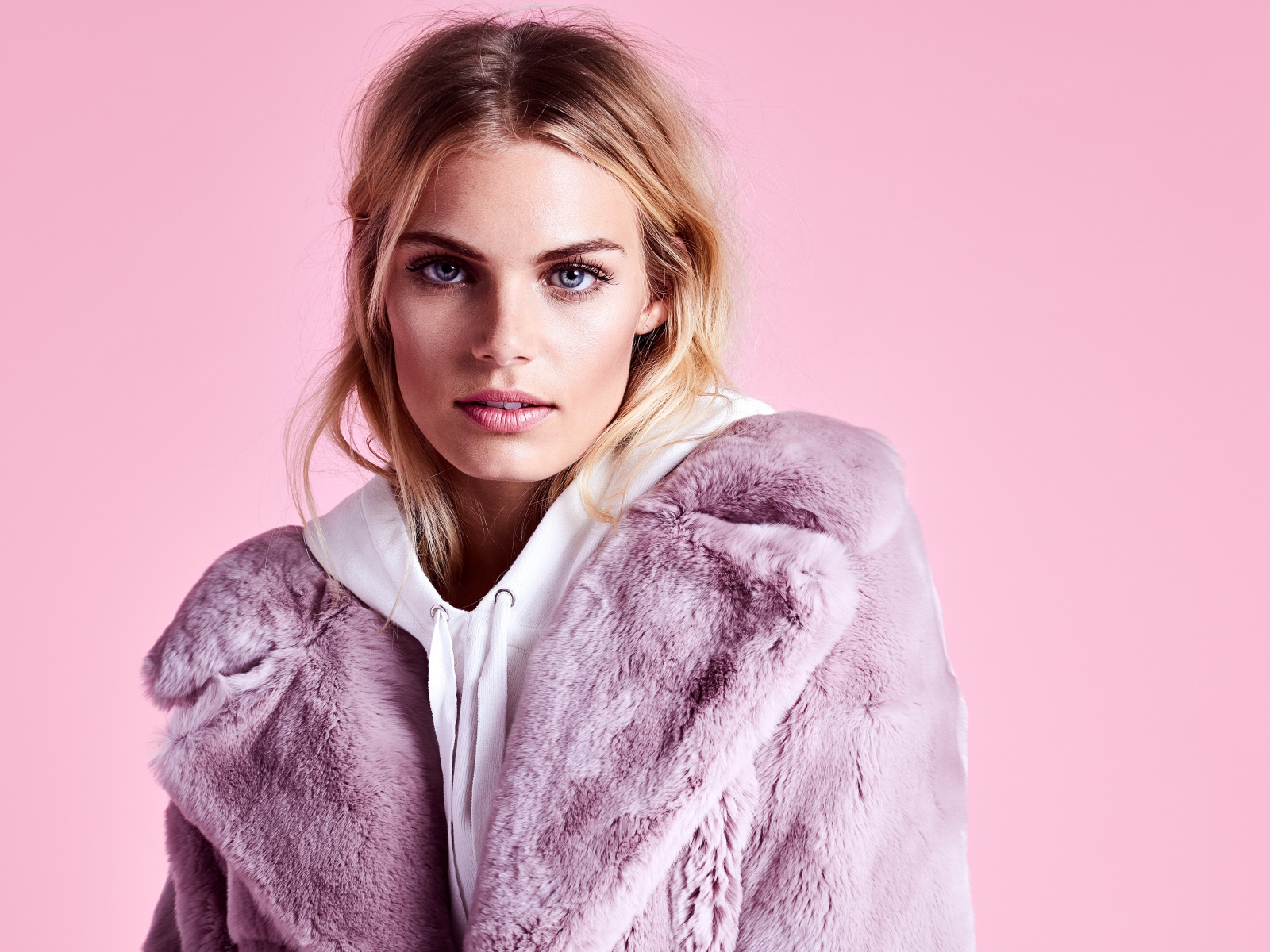 Красивая голубоглазая девушка в шубе на розовом фоне