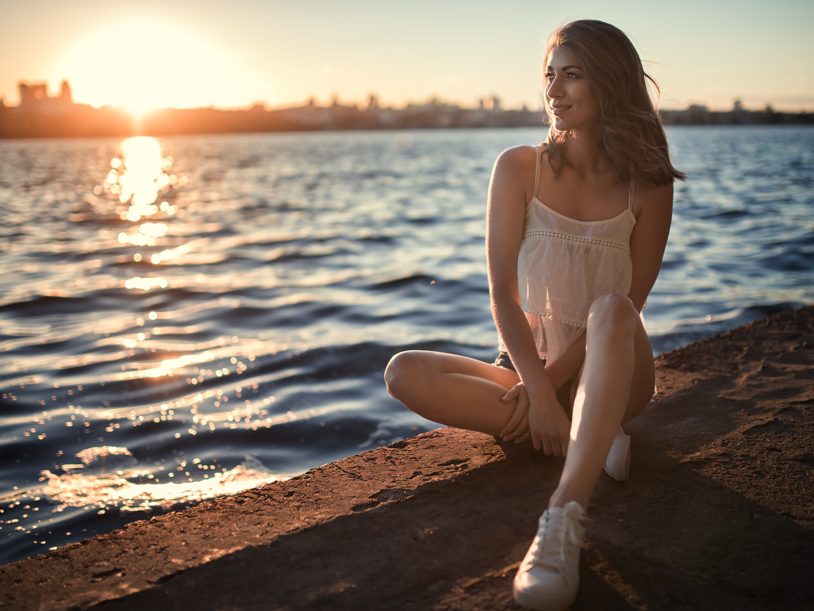 Красивая улыбающаяся девушка сидит в лучах солнца у реки