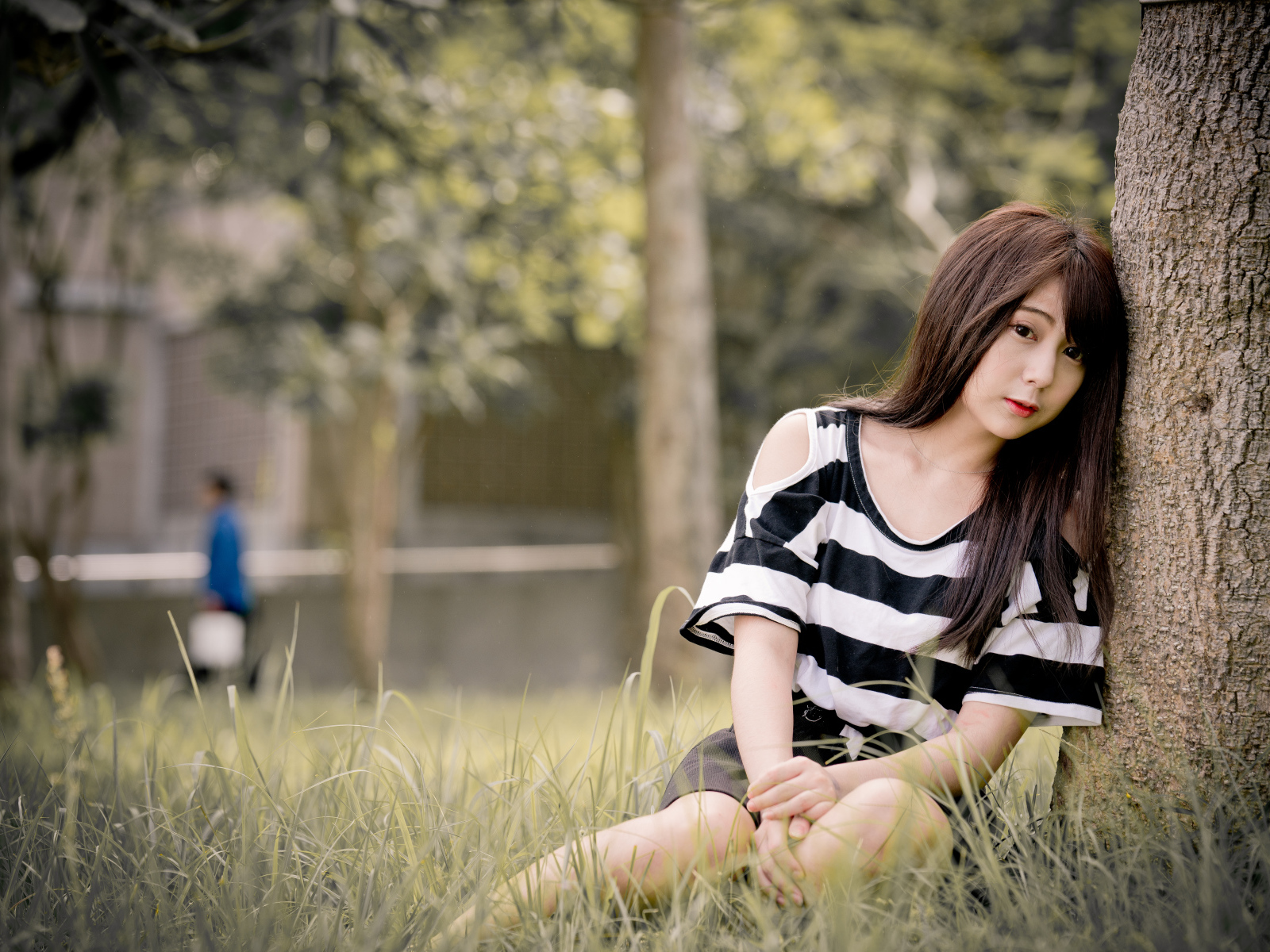 Молодая девушка азиатка сидит на траве у дерева