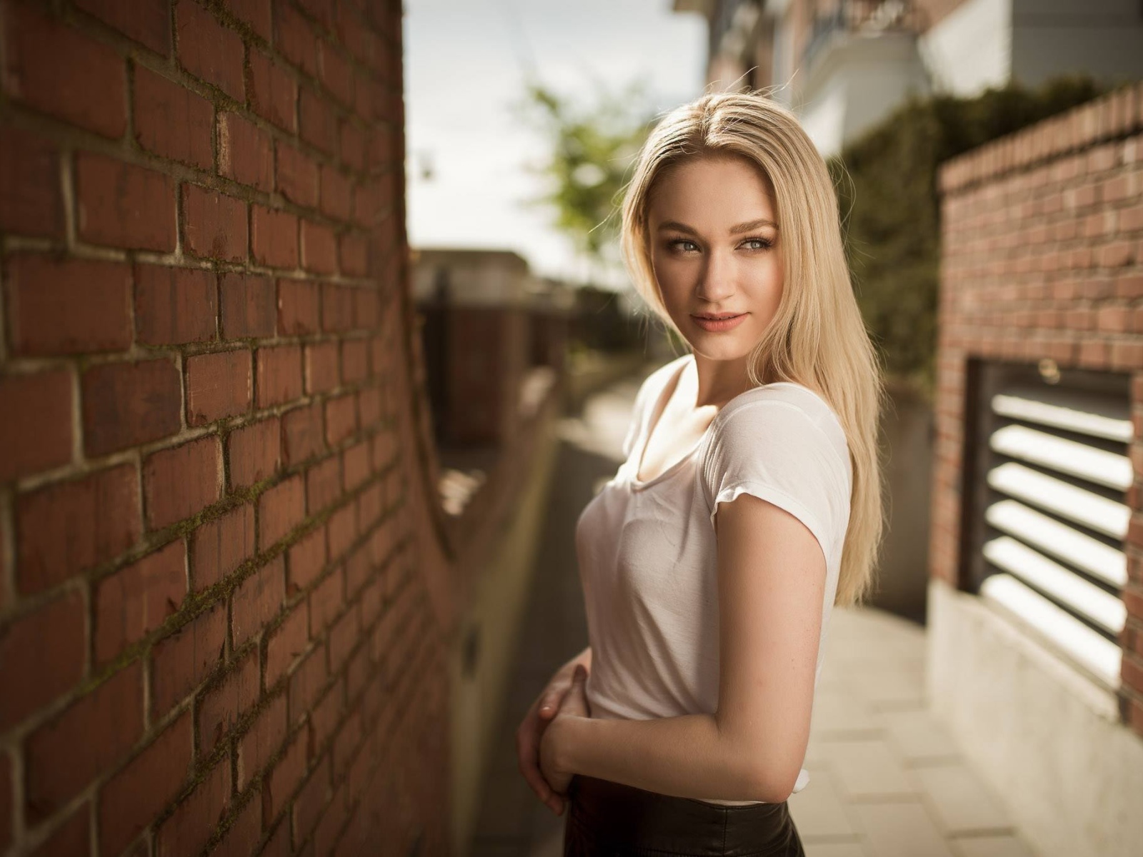 Молодая девушка блондинка у кирпичной стены 