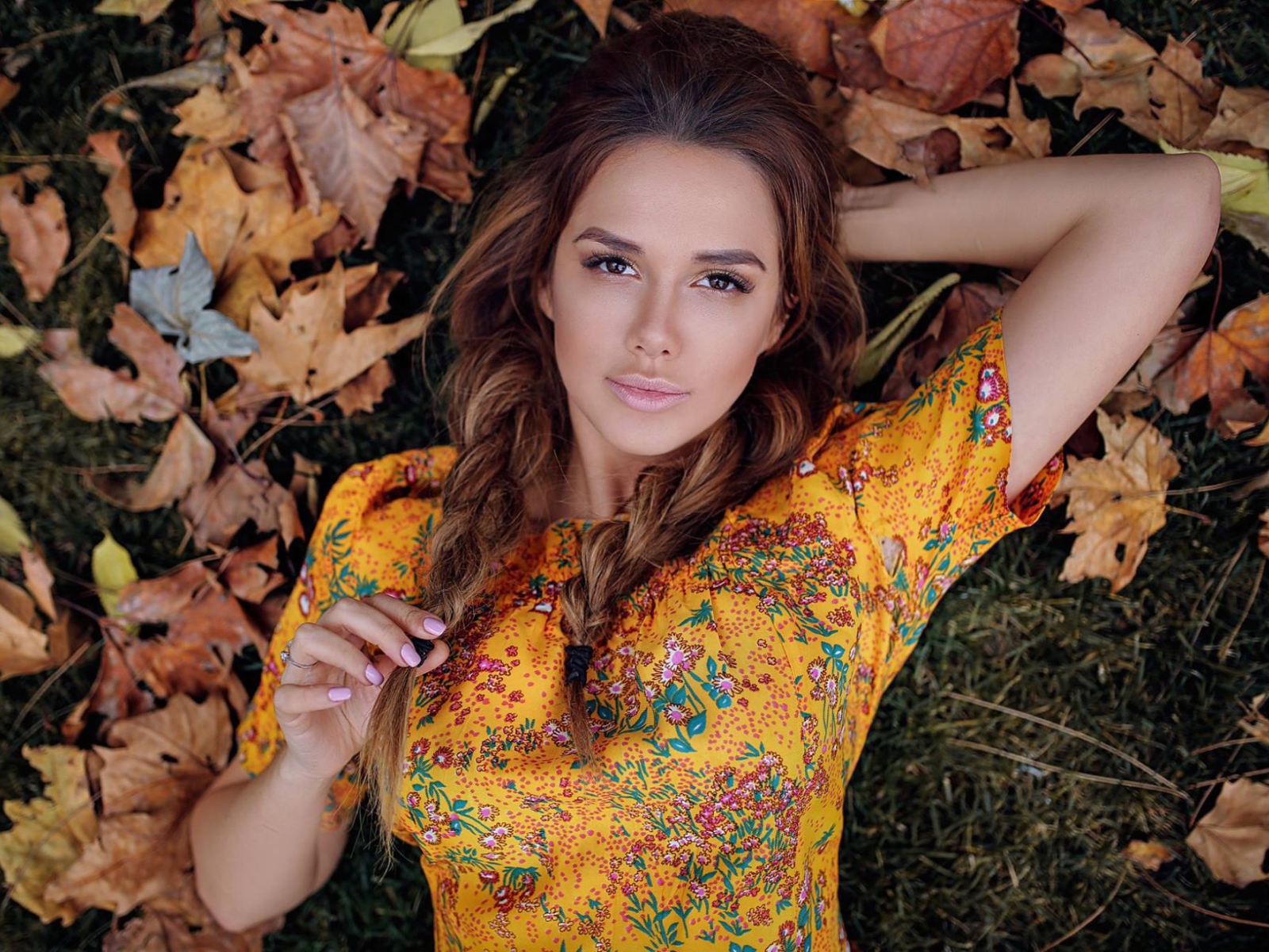 Молодая брюнетка лежит на траве с сухими листьями