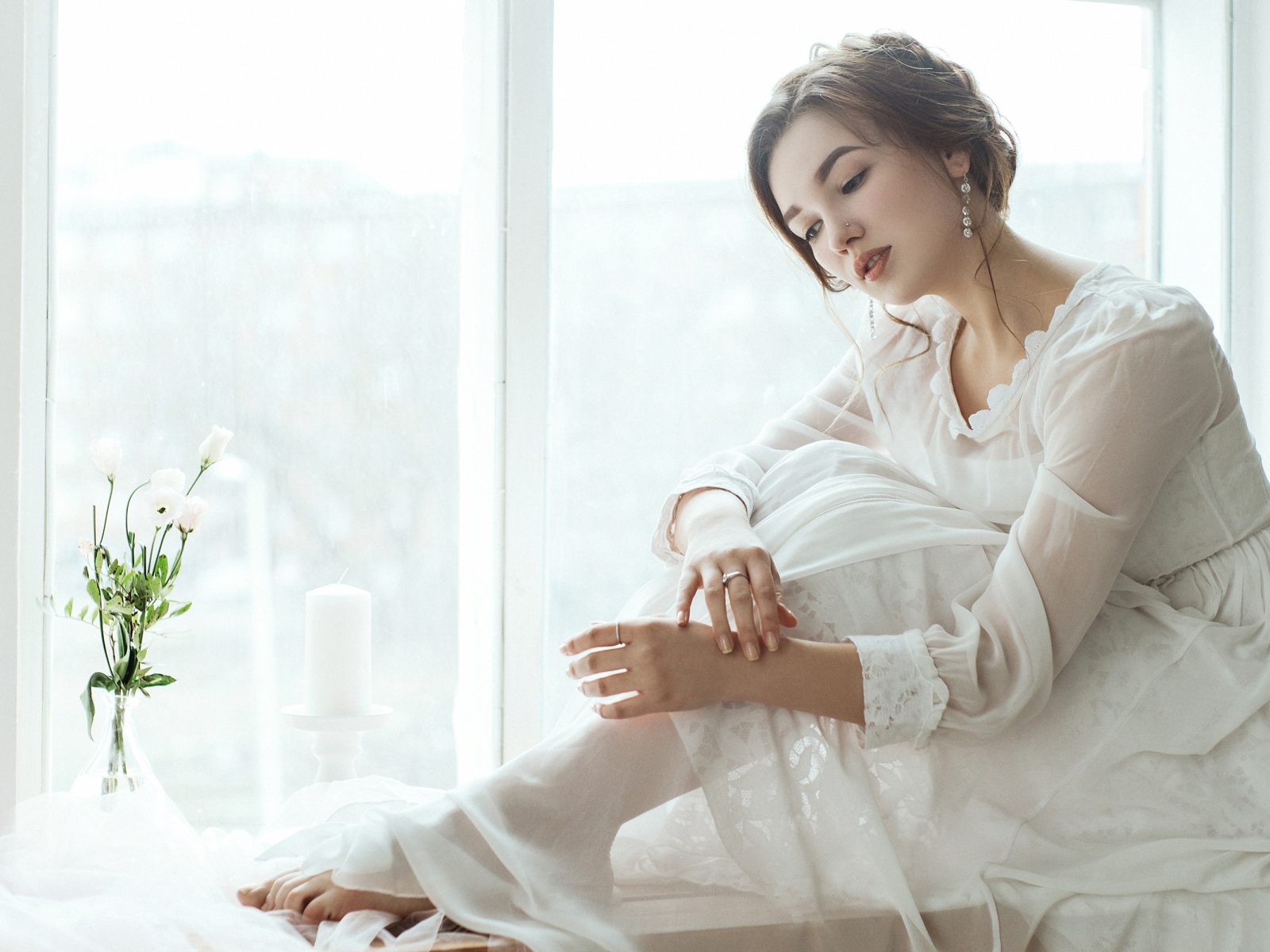 Молодая грустная девушка в белом платье у окна