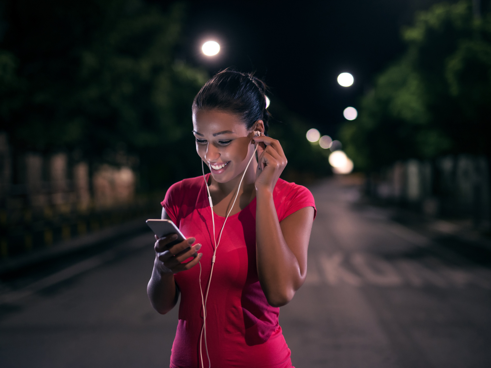 Молодая улыбающаяся девушка в наушниках с телефоном в руках