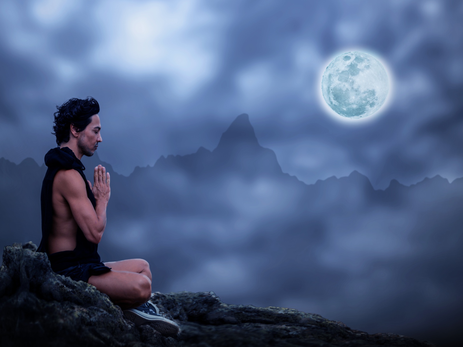 Мужчина медитирует на камне ночью в полнолуние