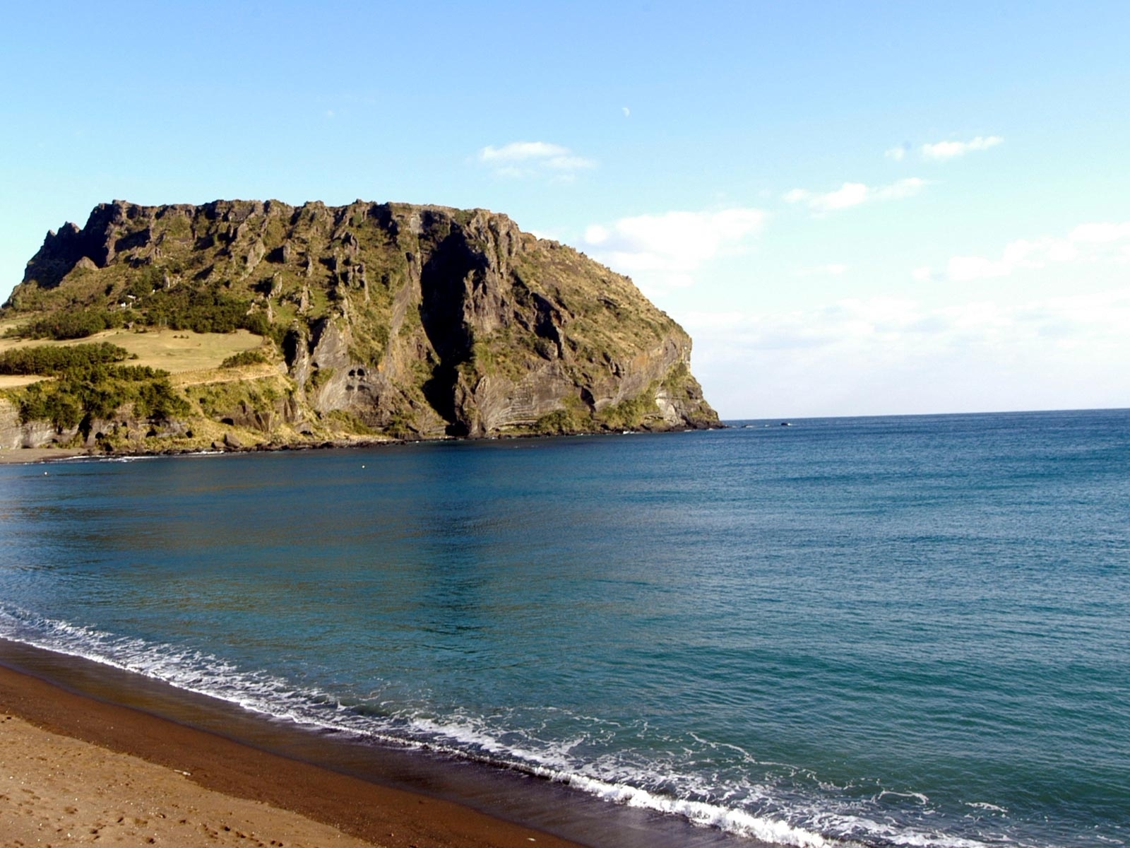 Гора на фоне спокойной воды моря под голубым небом